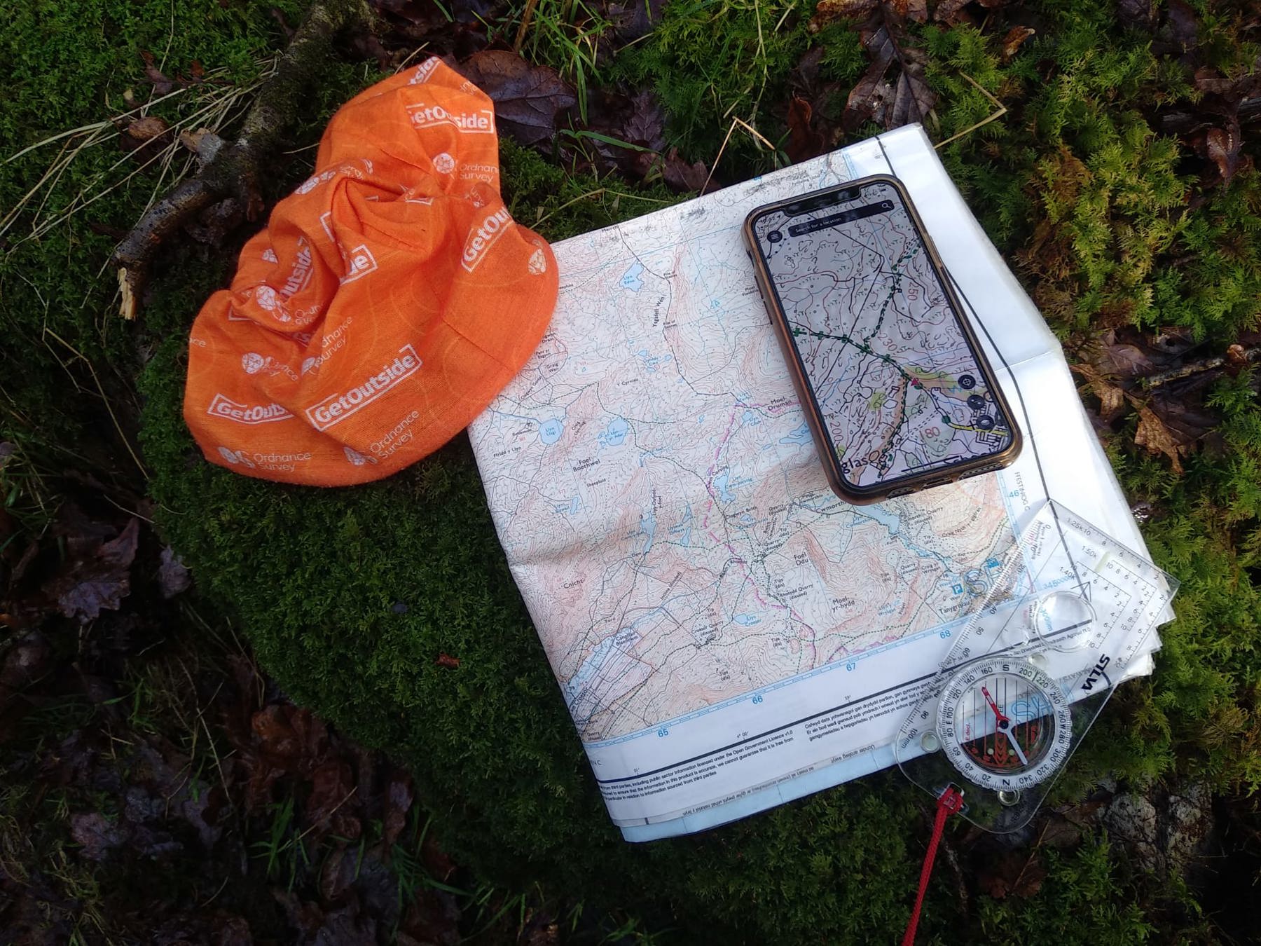 Mahroof’s map is on the ground, on top of some moss, levaes and bark. His compass and phone, with the digital mapping app open, are led on top.