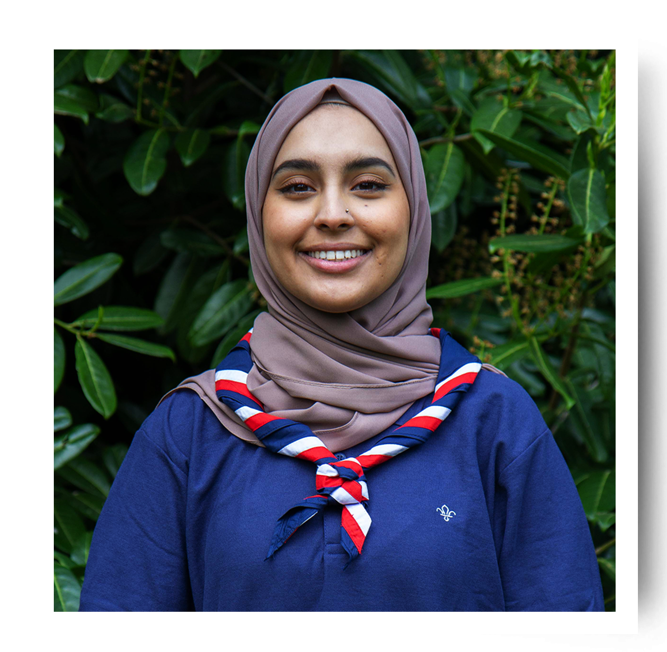 UK Youth Commissioner Ayesha Karim is wearing Scouts uniform and a necker, and is smiling outside in front of a hedge