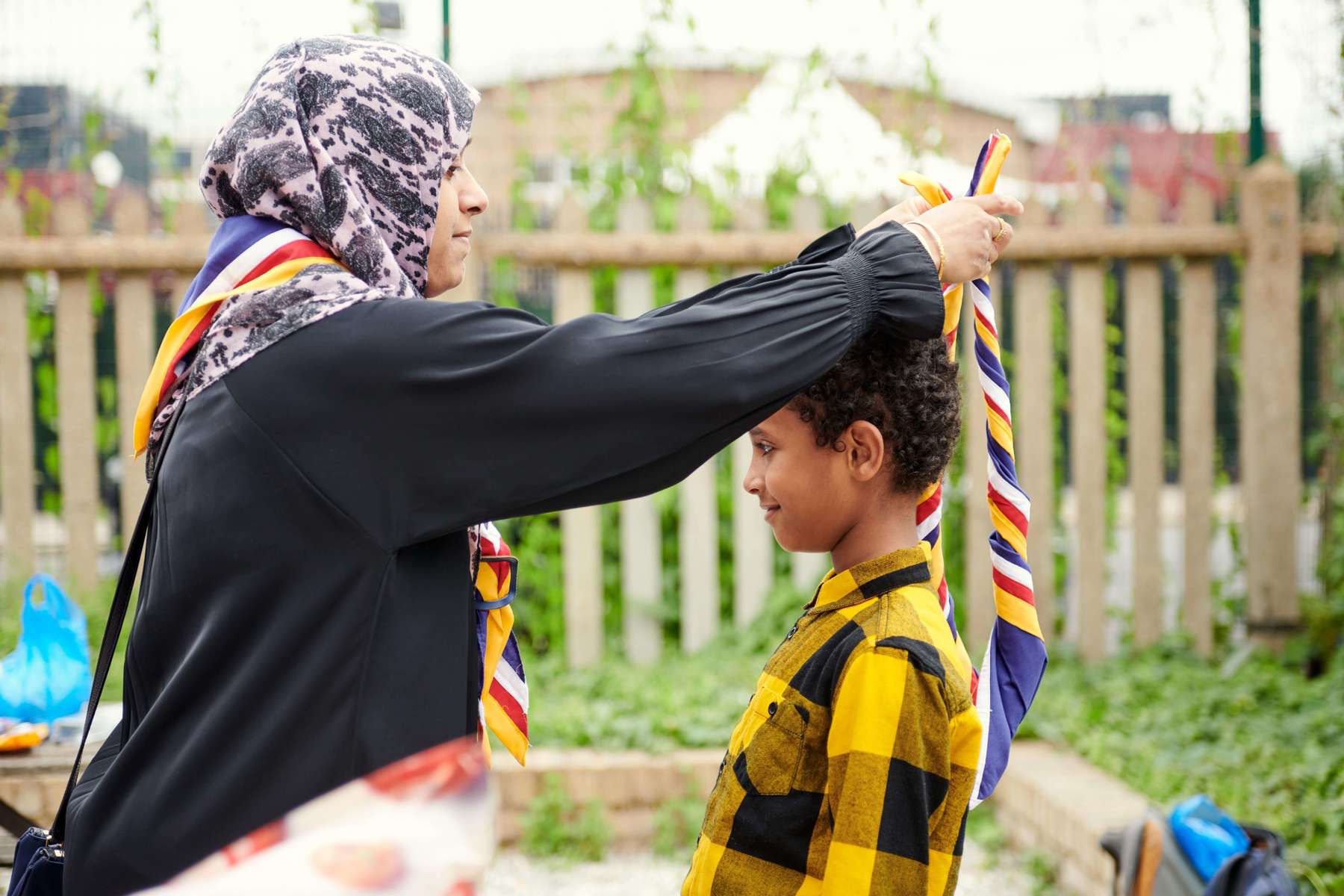 A volunteer places a white, red, yellow and blue scarf over the head of a young person.