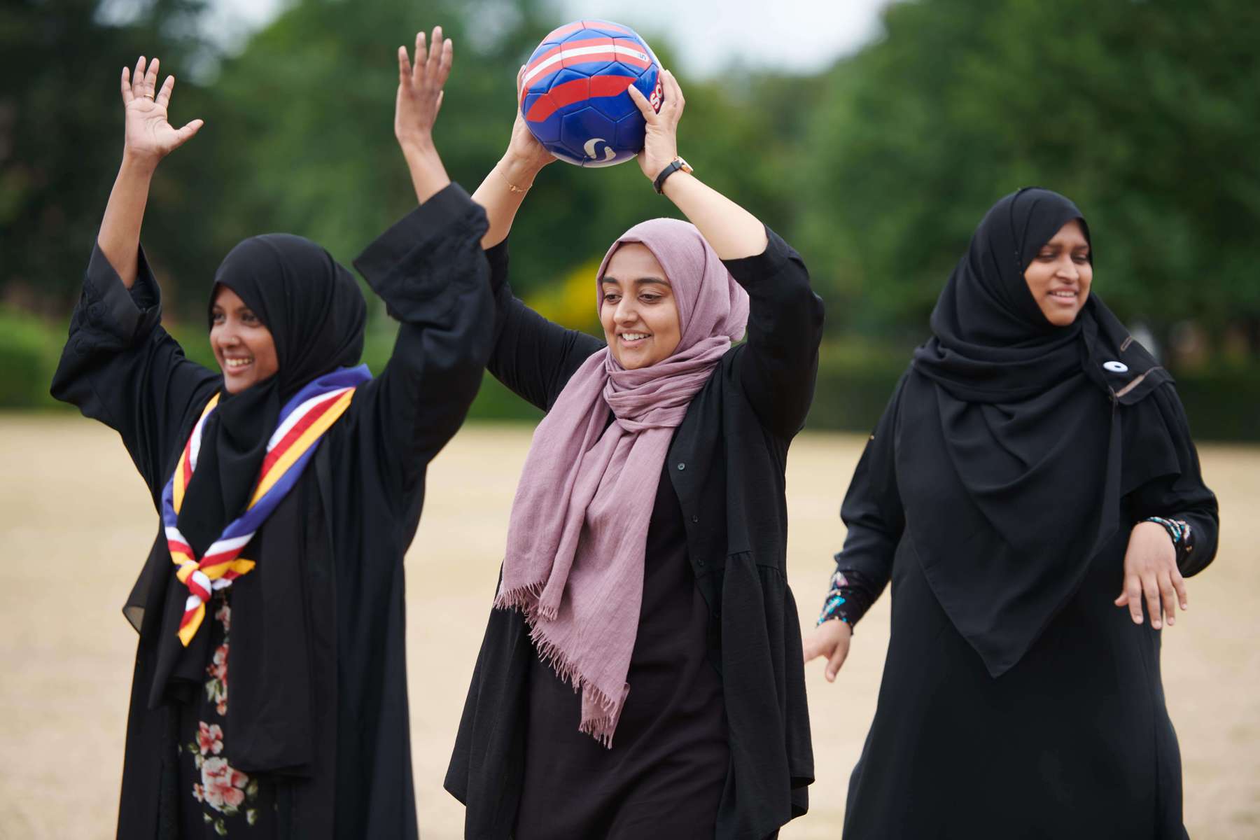 Three volunteers stand in a line, while the volunteer in the centre holds a football above their head.