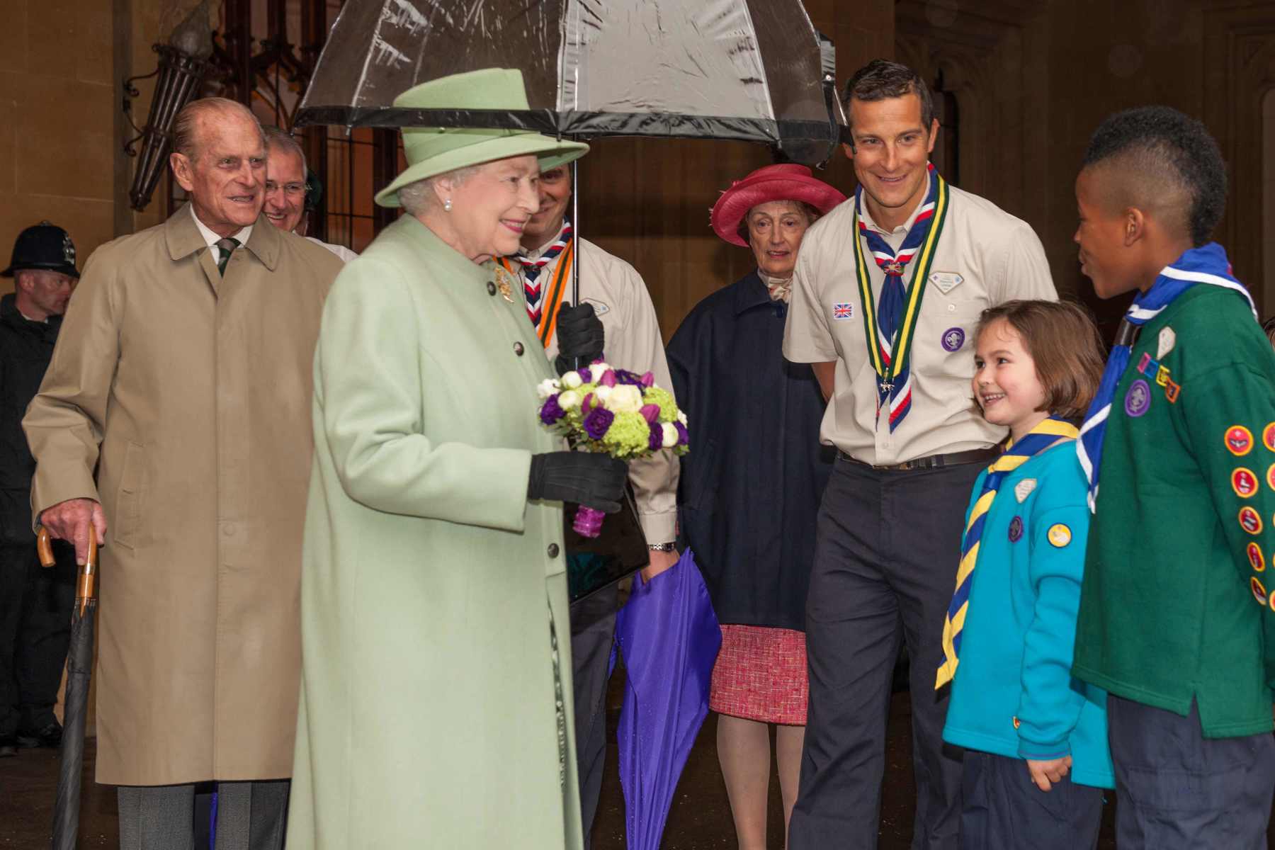 The Queen smiles at two young people while stood with Prince Philip and Bear Grylls.