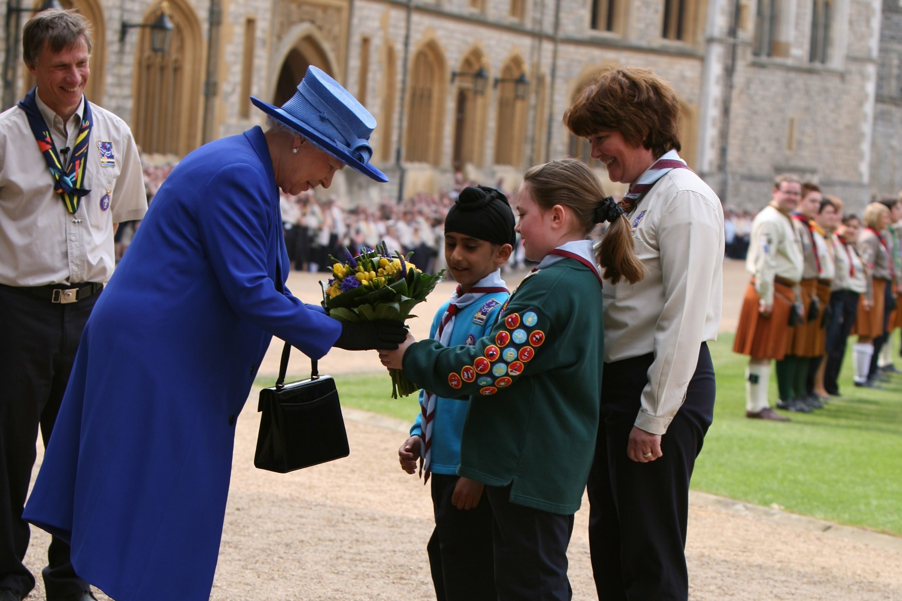 Two young people and a volunteer hand a bunch of flowers to the Queen.