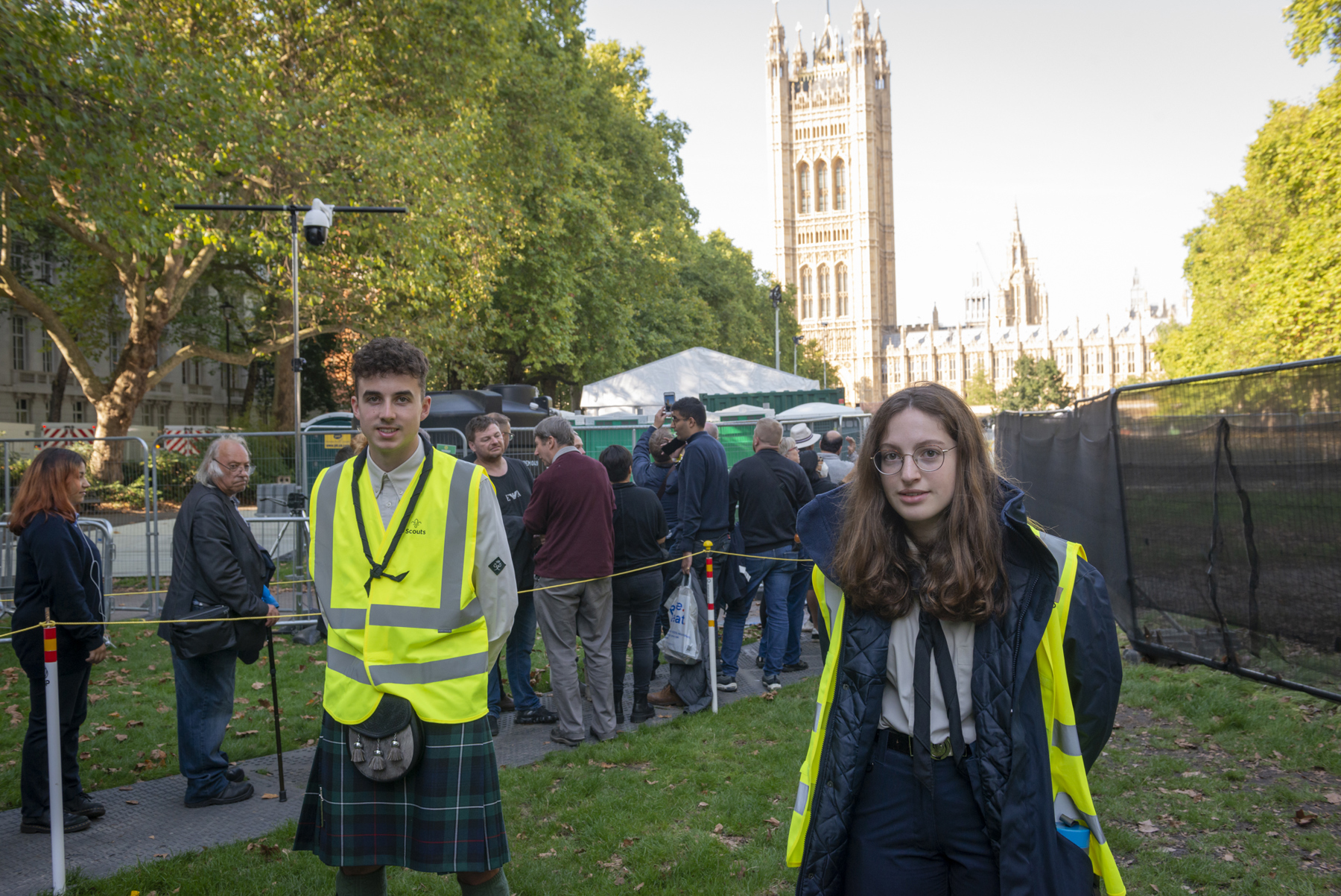 Two Scouts in hi-vis jackets smile at the camera while standing in front of Westminster Abbey.
