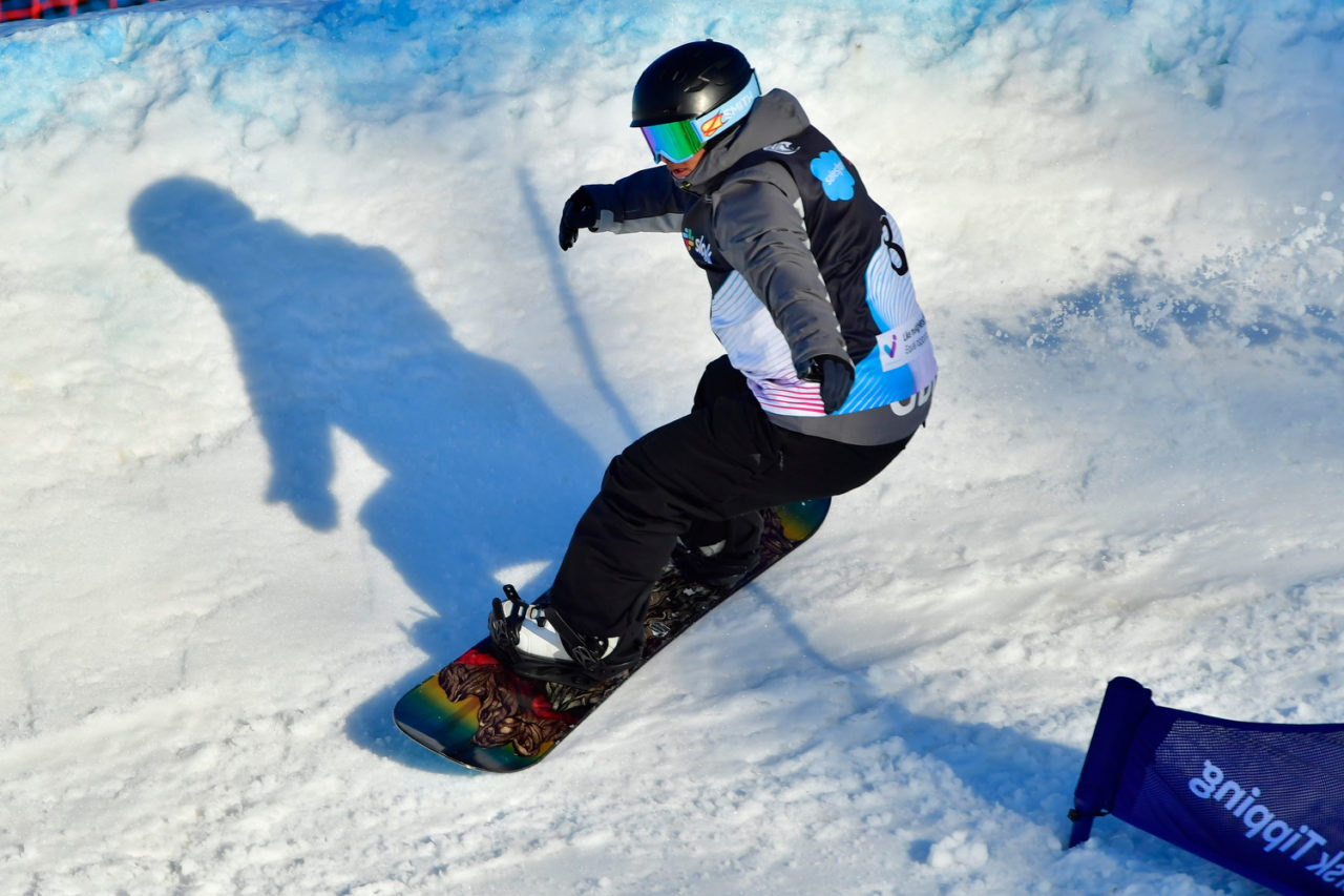 Nina is snowboarding on a snowy mountain, leaning slightly to the right with her arms stretched out.