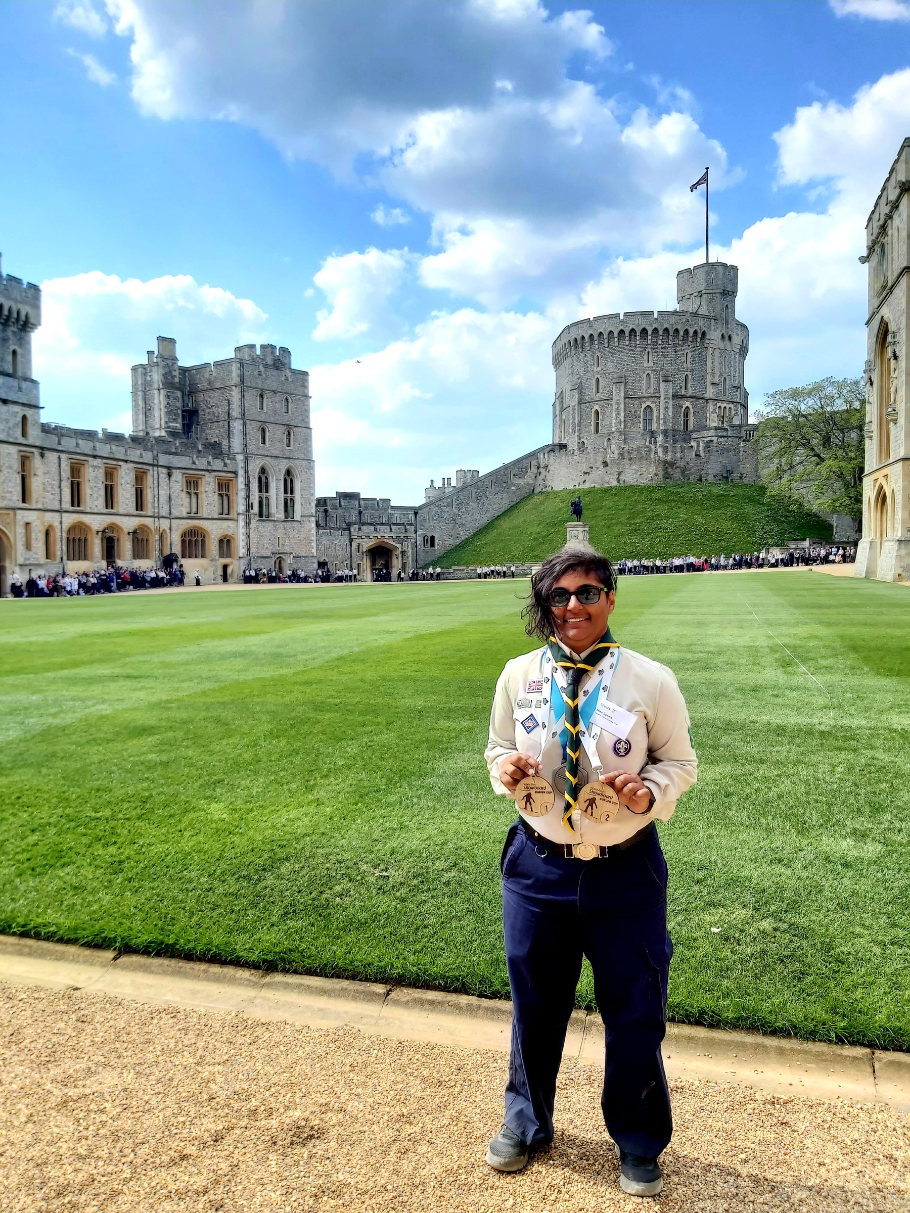 Nina is wearing her Scouts uniform and a necker, holding badges and standing on the gravel in front of Windsor Castle