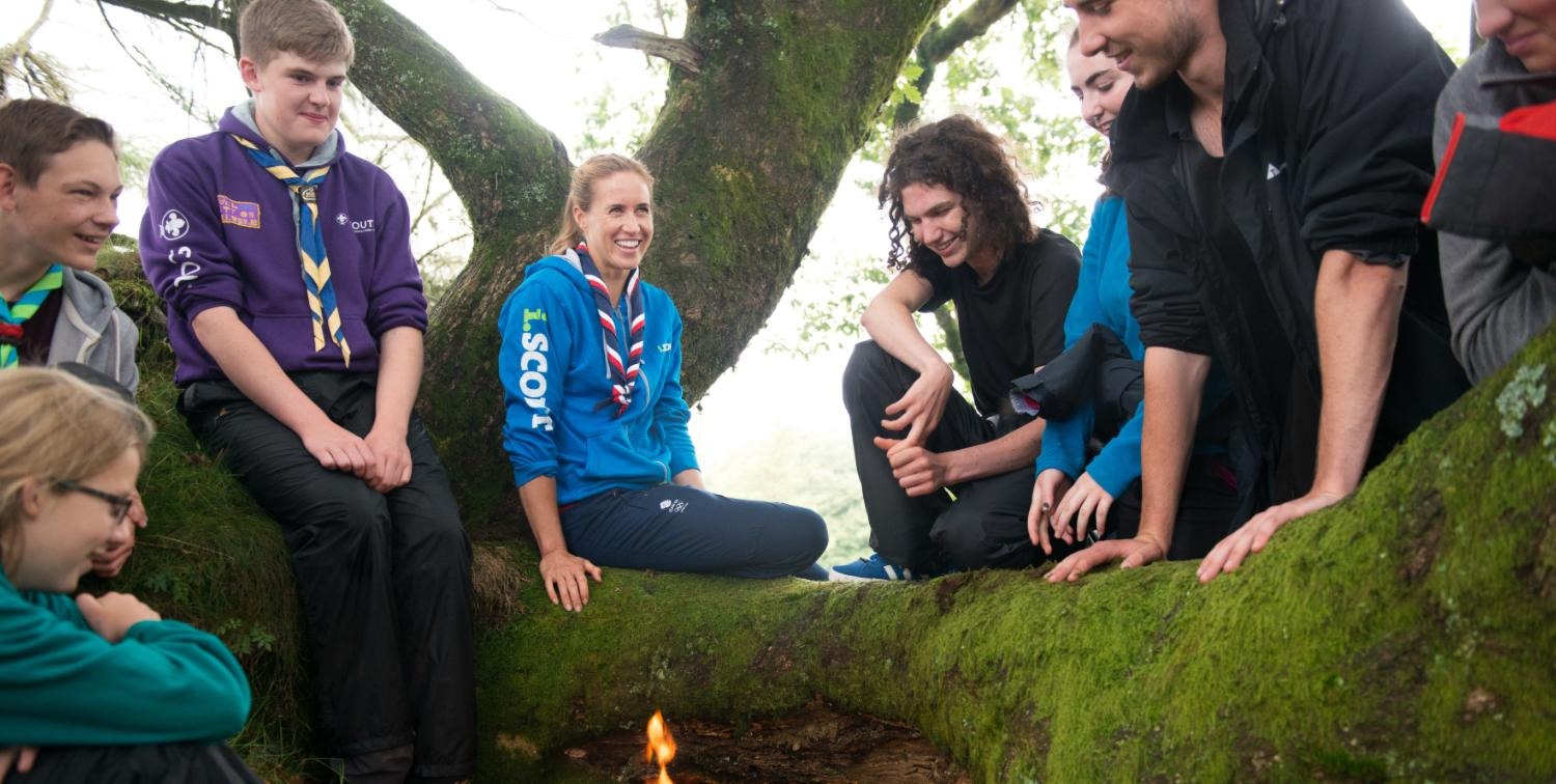 A group of Scouts and Explorers sitting on a tree talking and laughing.