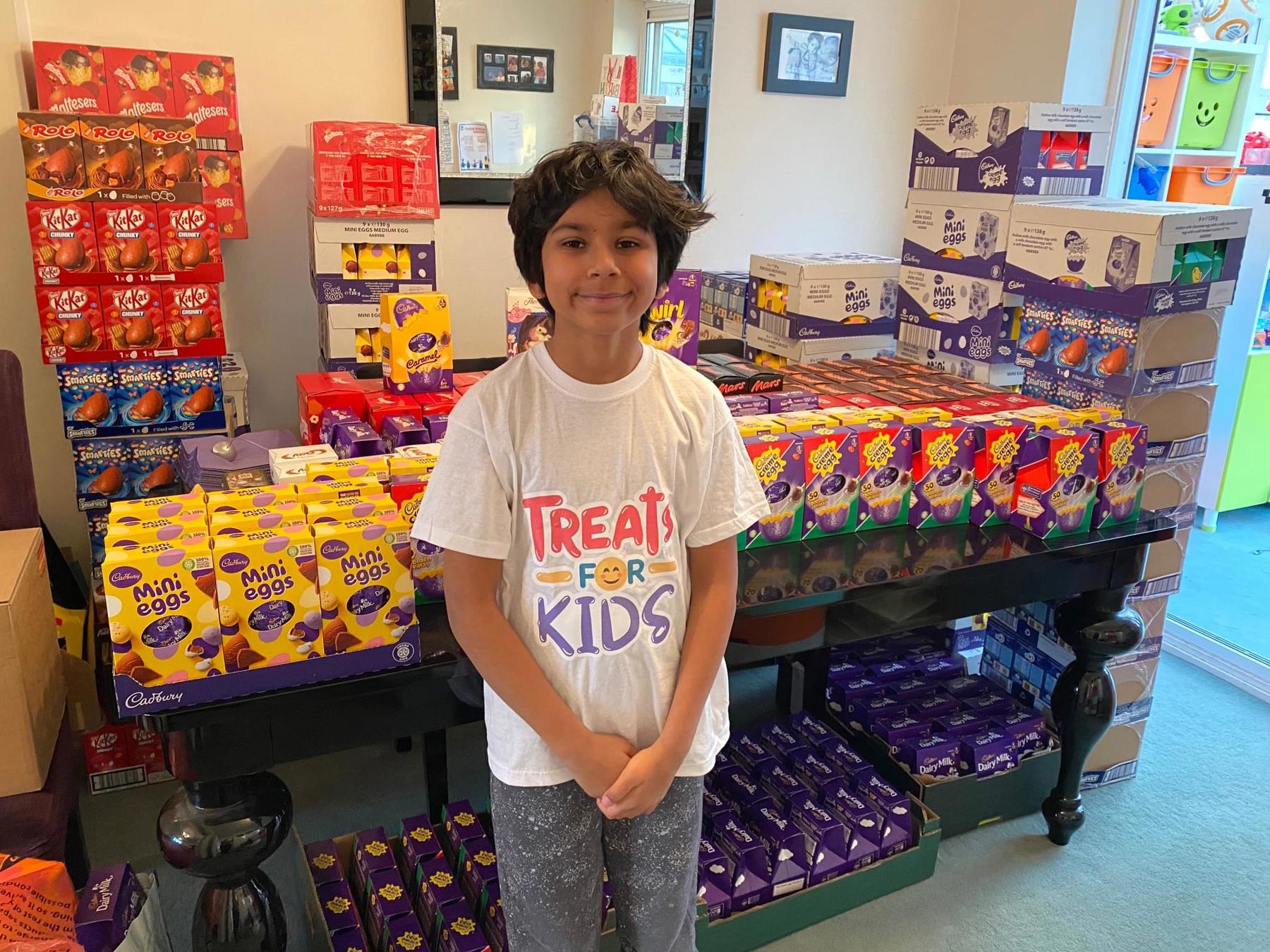 Neo is stood in front of lots of Easter eggs, and he is smiling. They are behind him on tables.
