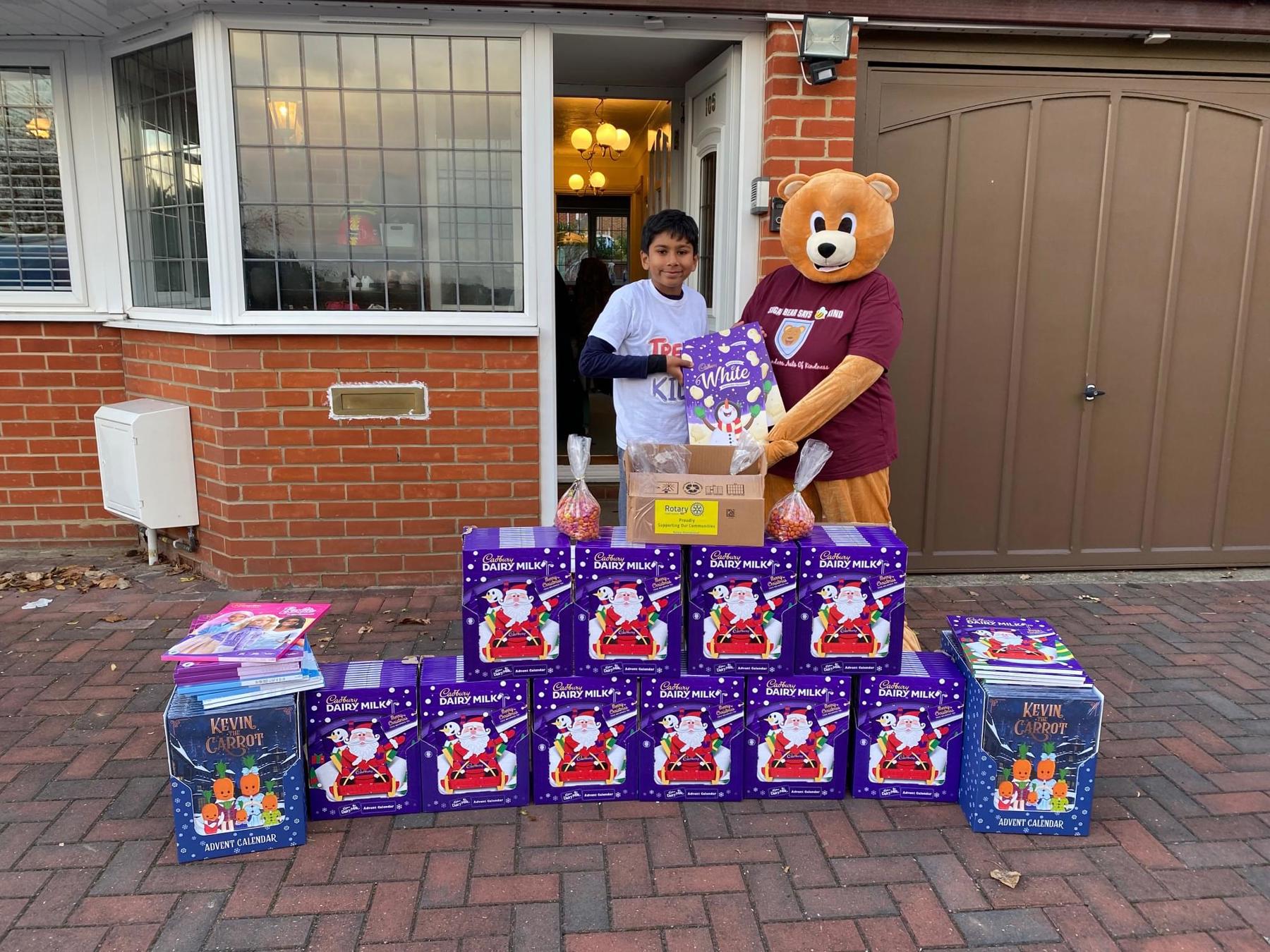 Neo is stood on the driveway with a teddy bear mascot with lots of advent calendars that have been donated.