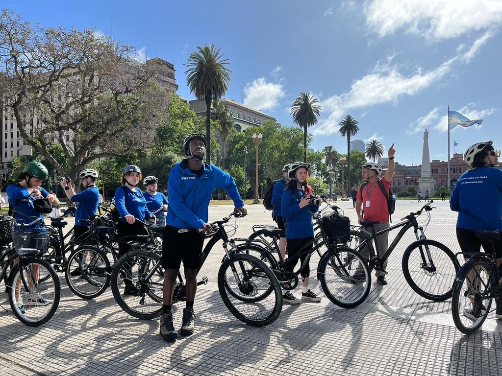 Dwayne Fields and young people on the WeTwo expedition are standing with bikes in blue t-shirts and jackets on pavement in Buenos Aires