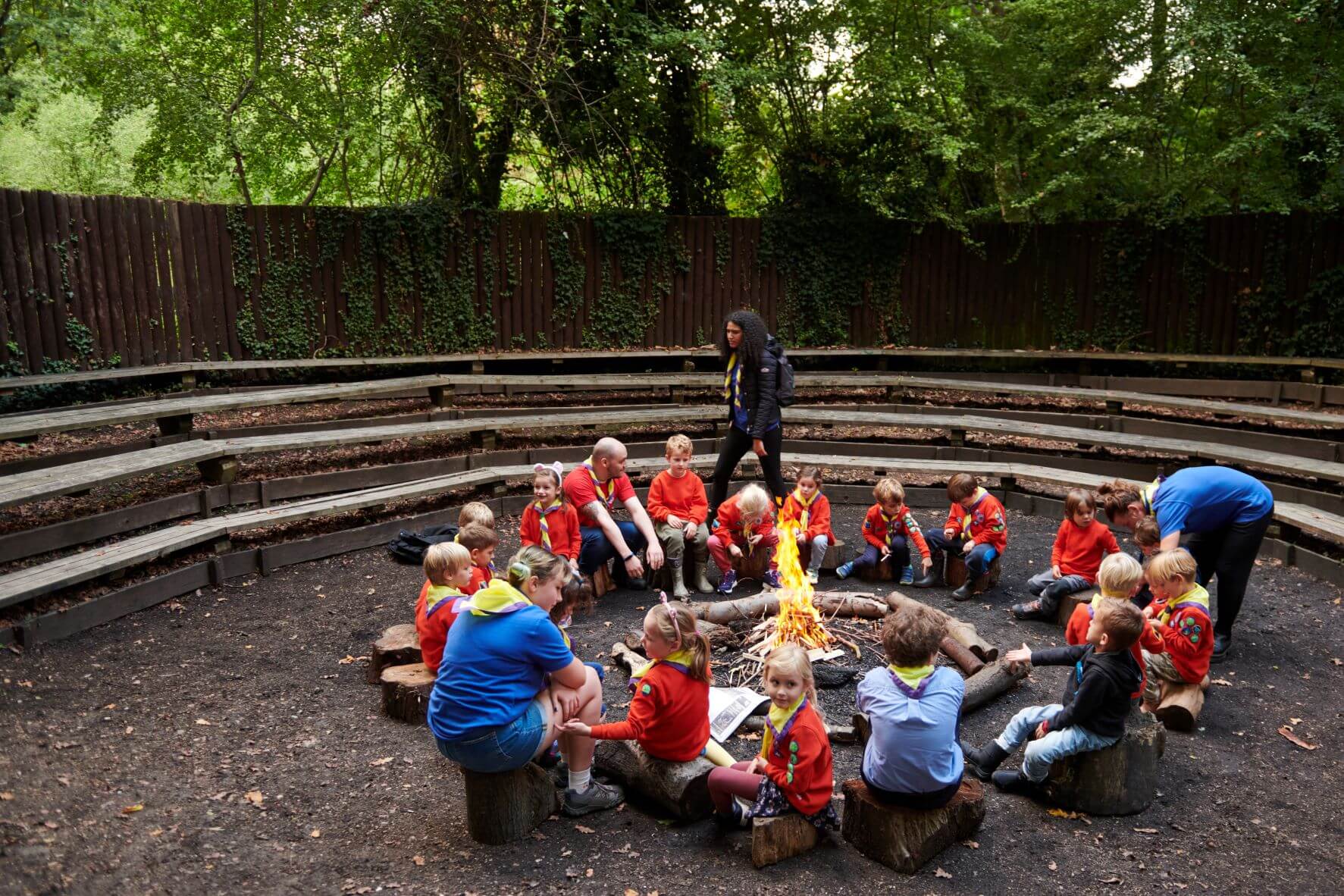 A group of Squirrels and volunteers sit in a circle around a campfire.