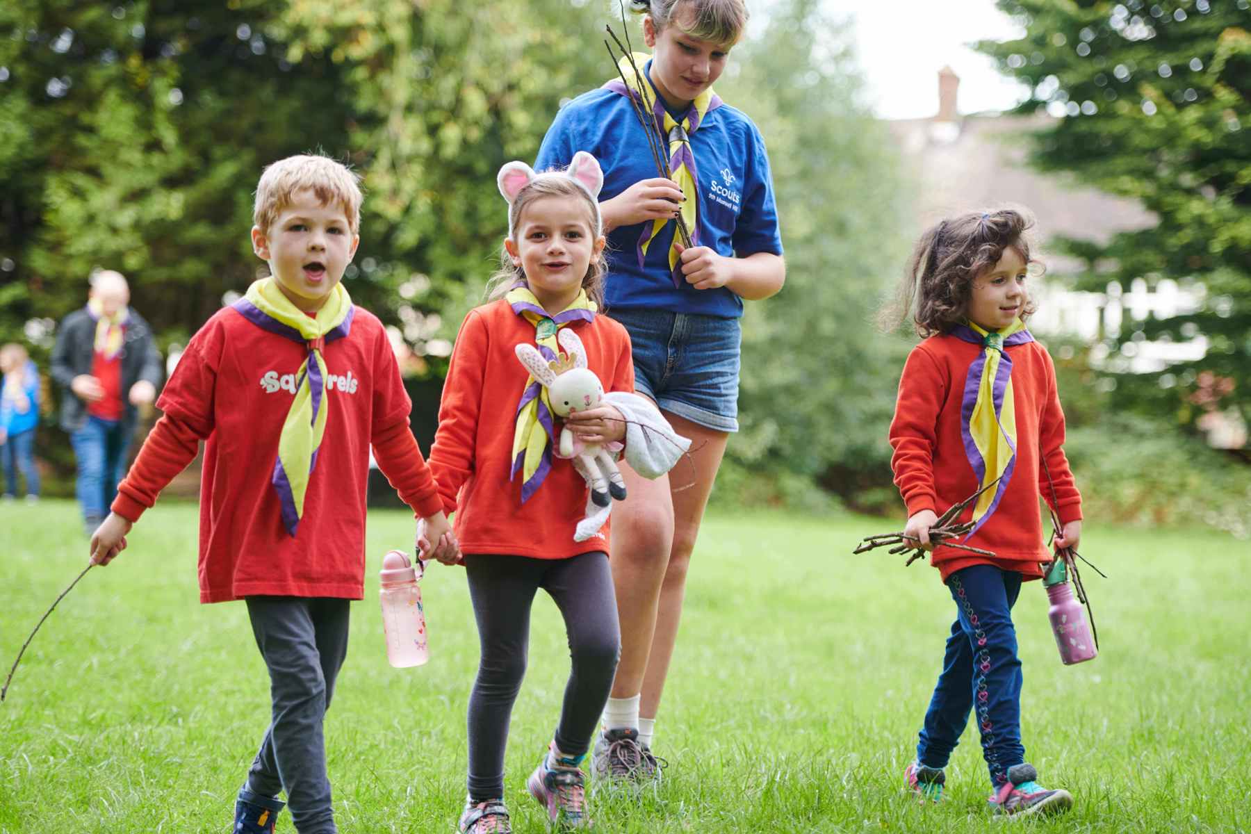 Two Squirrels wearing red jumpers hold hands while walking with another Squirrel and a Scout.