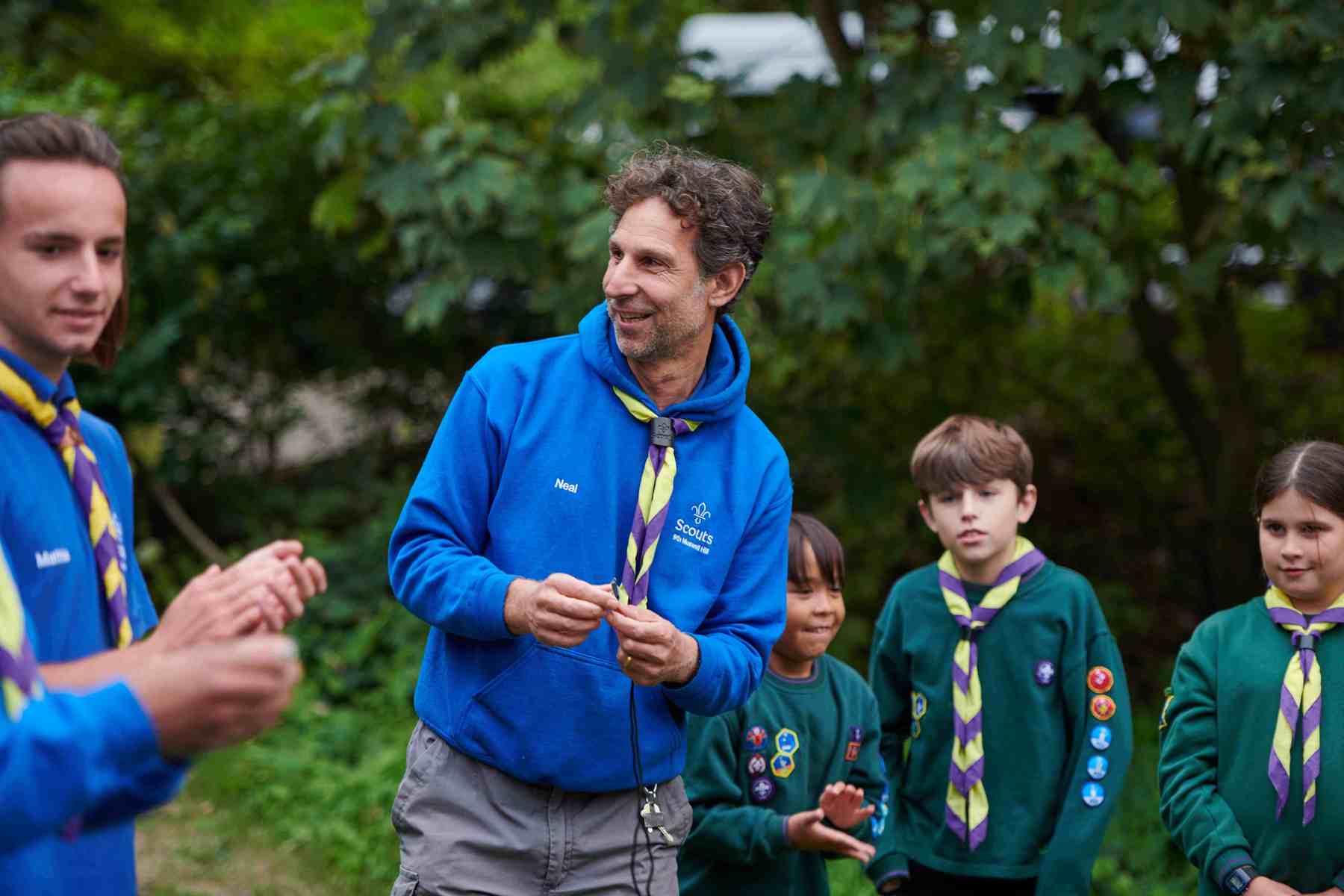 Two volunteers wearing bright blue jumpers stand outside with three Cubs in green uniforms.