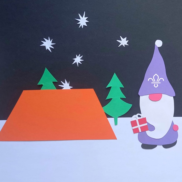 The image is made from coloured card with an orange tent, green Christmas trees and an elf with a purple hat showing a fleur de lis and a long white beard, all standing on white card as snow. There's a dark sky with white paper stars.
