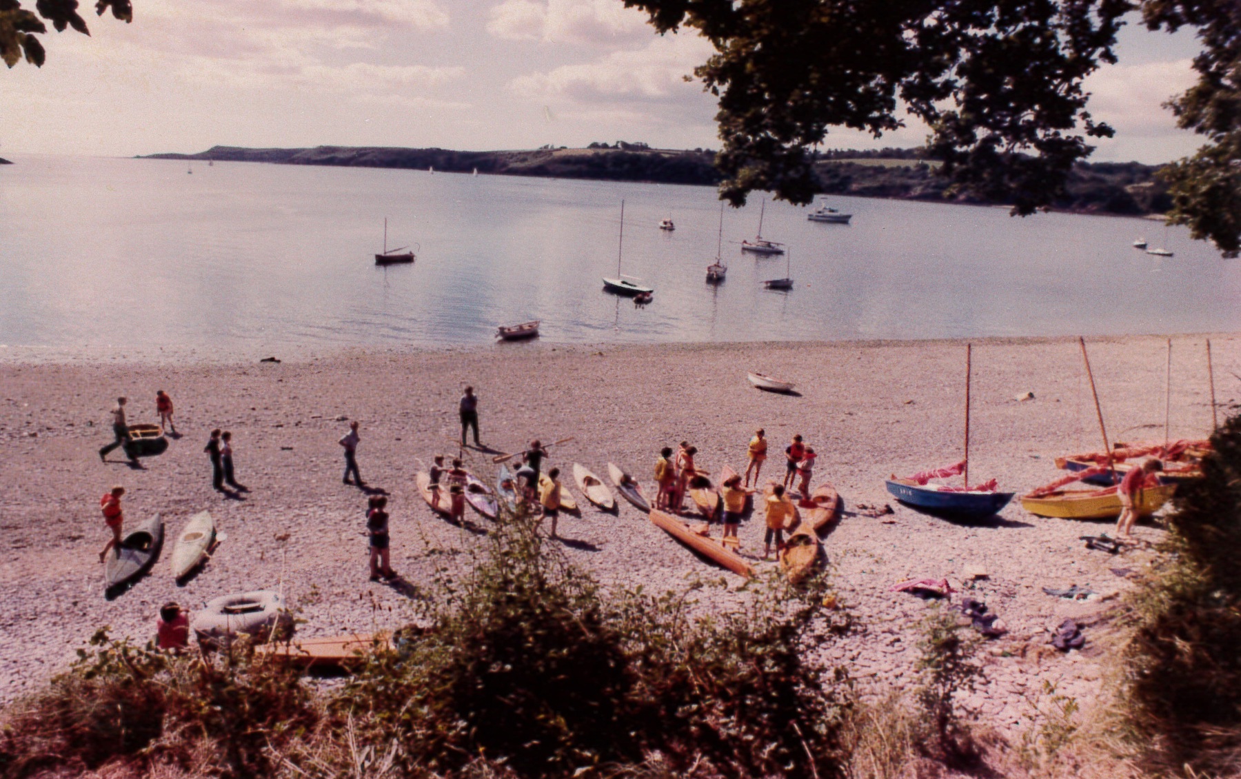 The photo shows a beach with lots of rowing boats on the sand and in the water. There are people in the distance gathered around the boats.