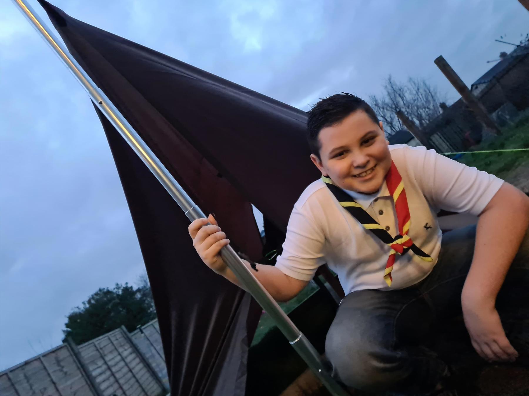 Leo sat outside his tent in the early evening in front of a cloudy sky. He's wearing his Scouts necker.