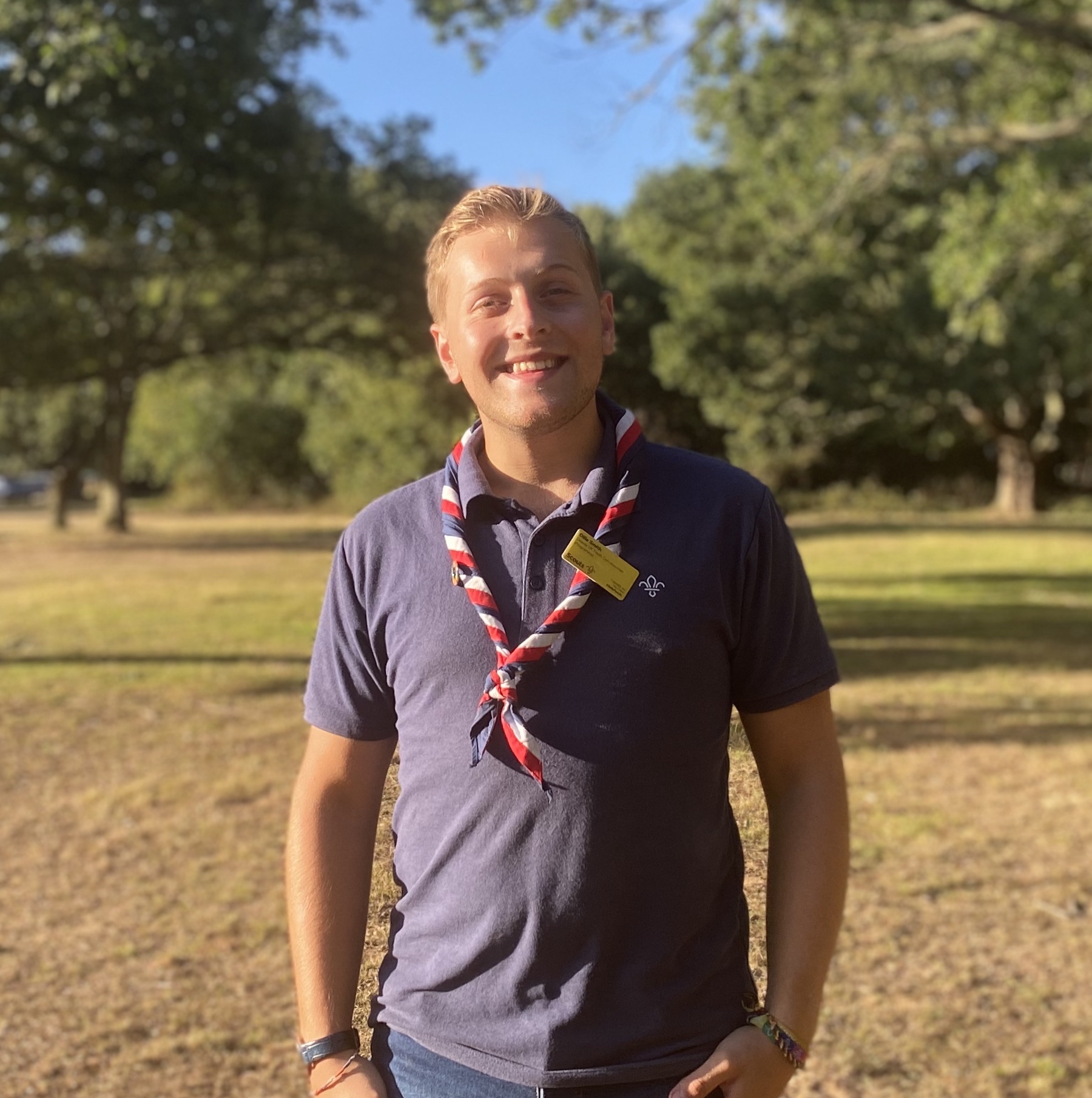 Ollie Smith smiles at the camera wearing Scouts t shirt and necker with outdoors background 