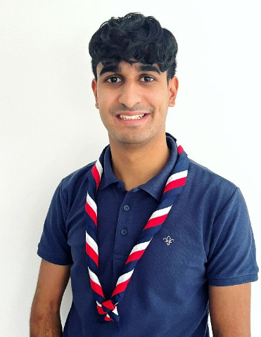 Nirav Patel smiles at the camera wearing navy Scouts t shirt and necker
