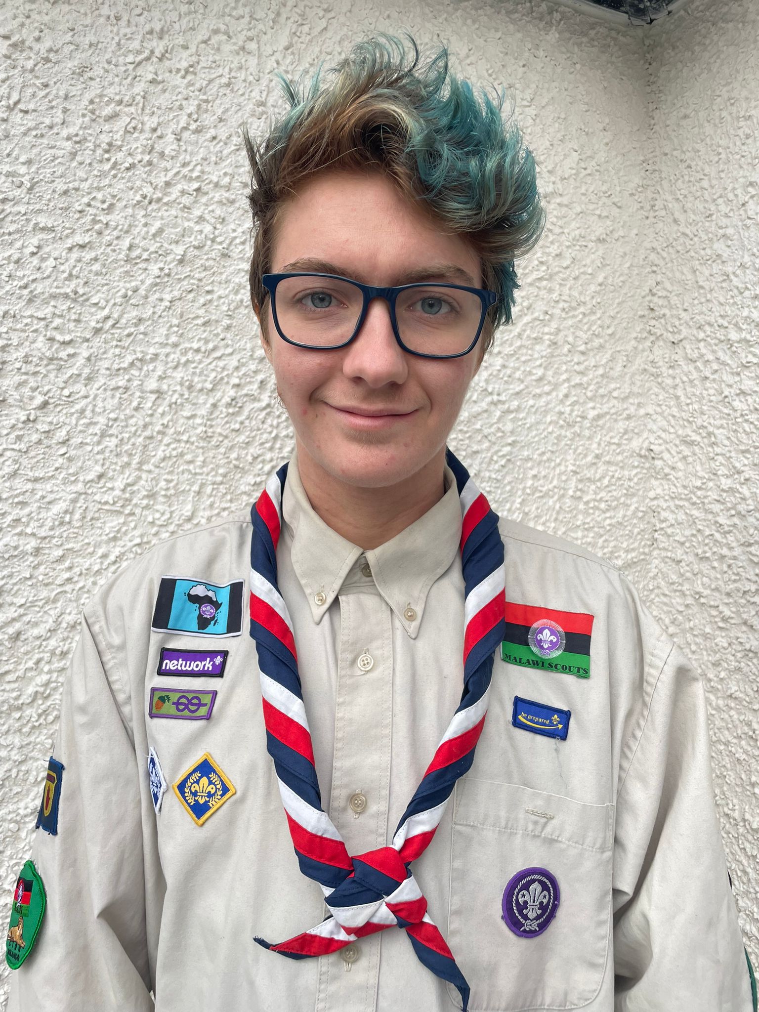 Jackson is smiling at the camera, wearing a volunteer uniform and the Scouts necker. Jackson has blue hair and glasses.
