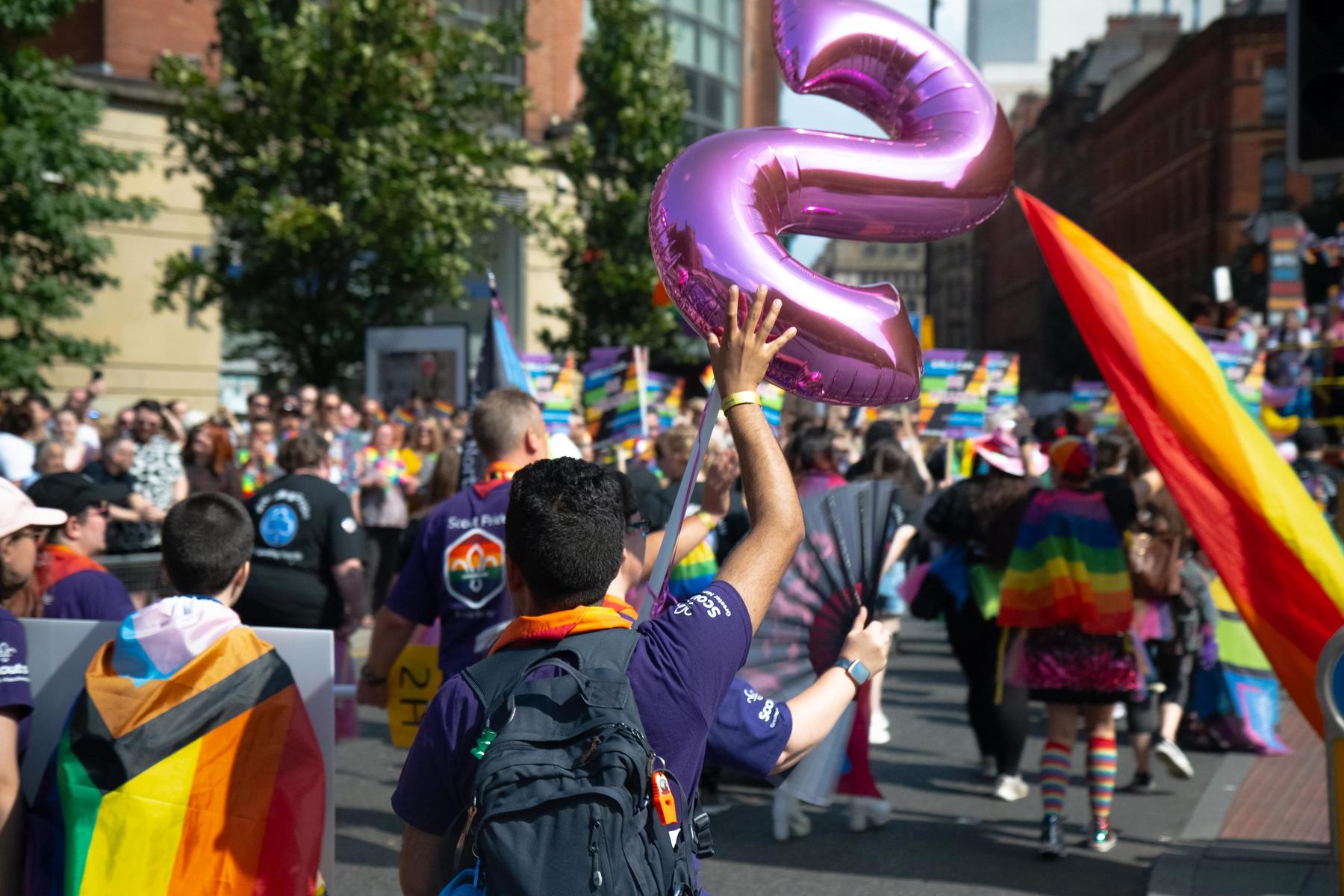 Scouts participating in Pride march, they are facing away from the camera and are wearing rainbow neckers.