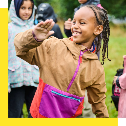 A young person looks to the side and smiles while waving