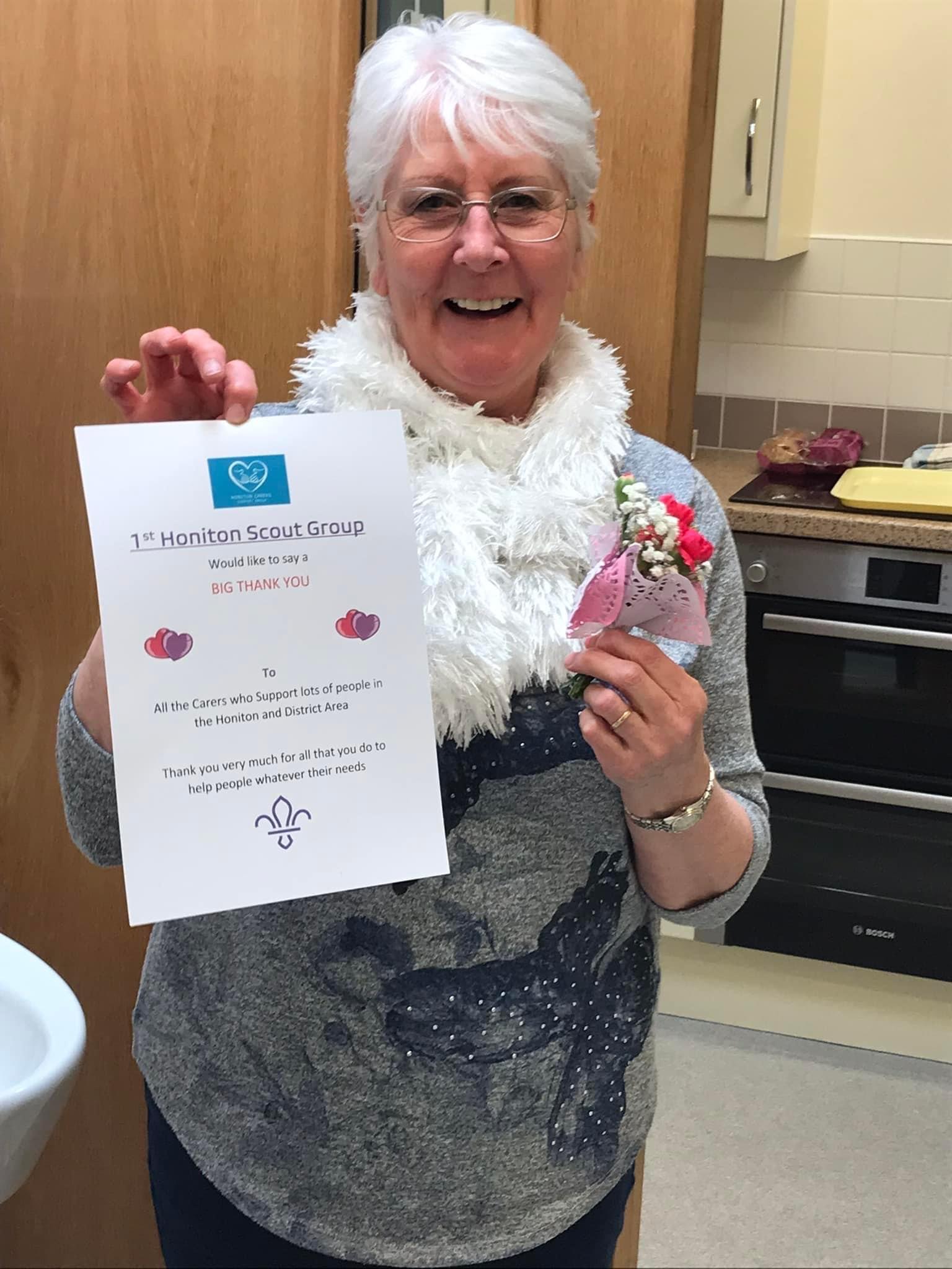 Val smiling at the camera and holding the carers certificate and small bunch of flowers given to each carer