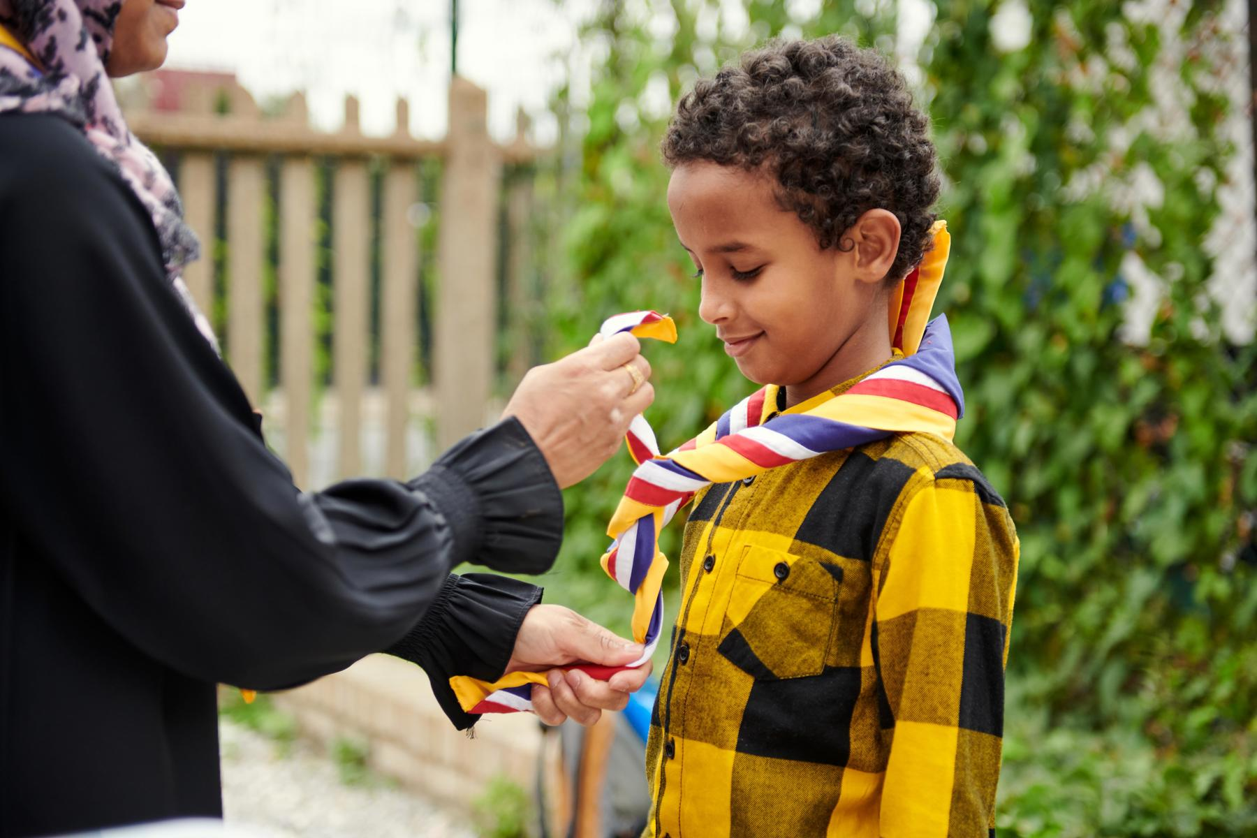 A young person is wearing a necker while an adult ties it for them