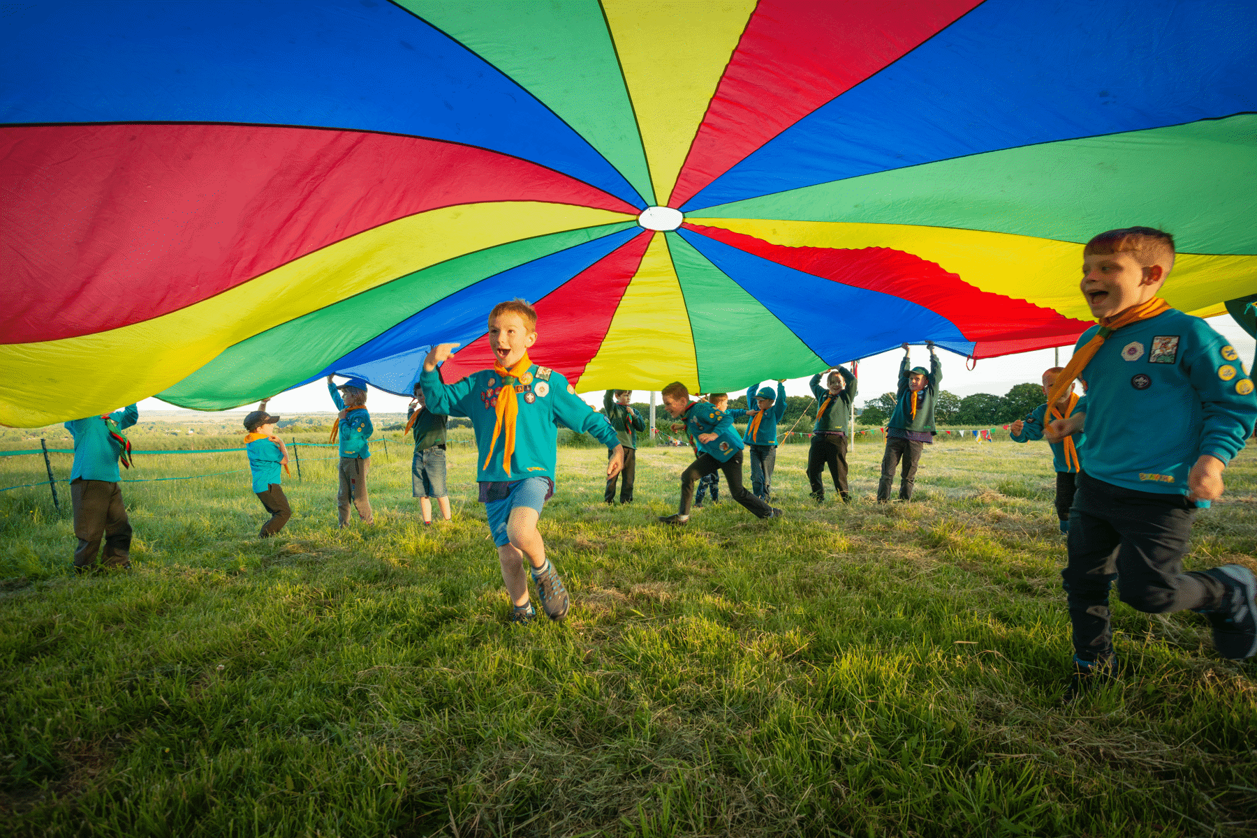 Cubs and Beavers running under a parachute on a field