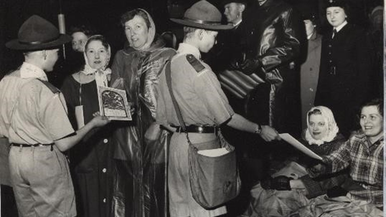 Black and white photo of two Scouts selling programmes for the Coronation to ladies sitting down