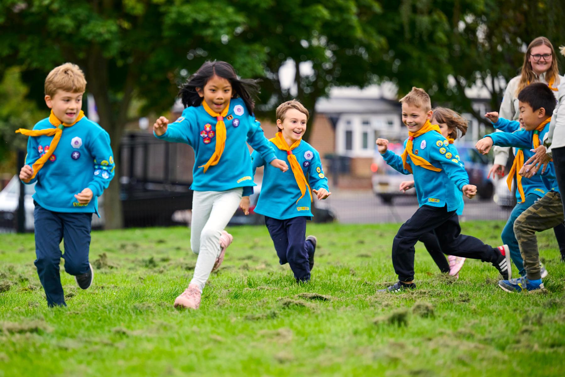 A group of Beavers in blue jumpers and yellow neckers run across grass while playing a game.