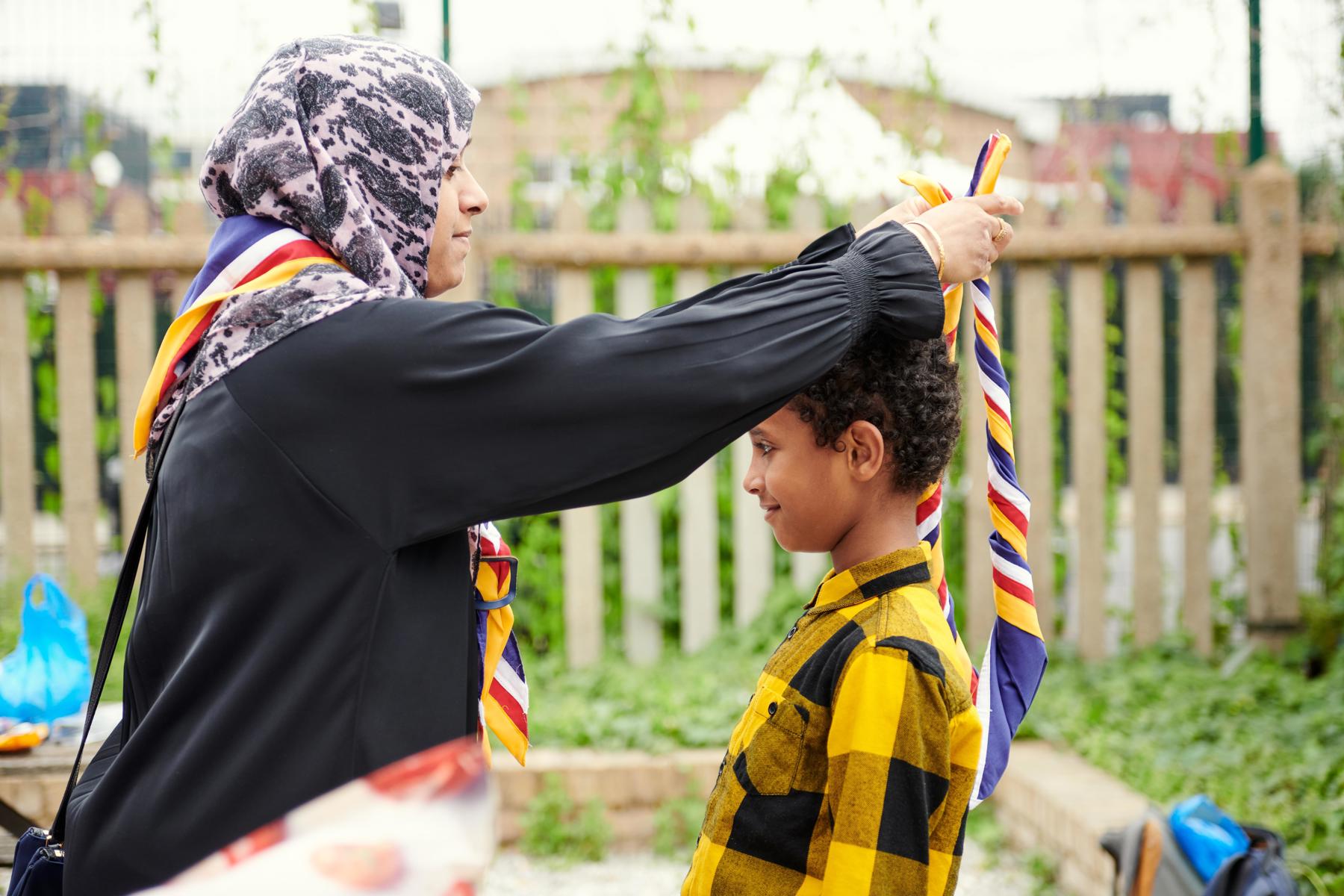 A volunteer places a yellow, red, blue and white necker around the neck of a young person.