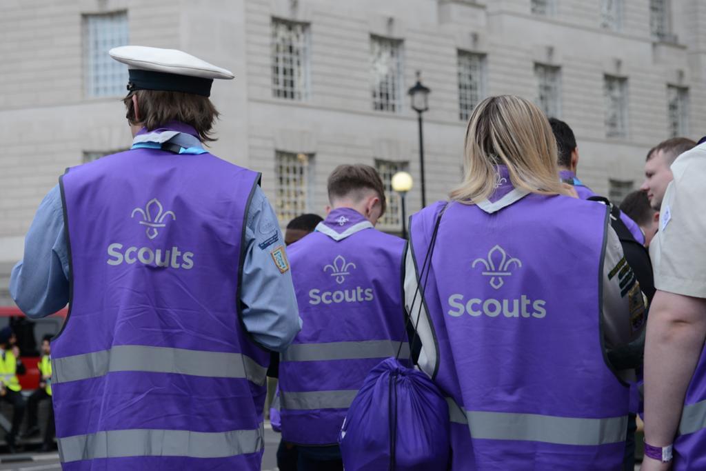 Three Scouts wearing purple high visibility jackets with the Scouts Fleur de Lis on walking in the streets of London