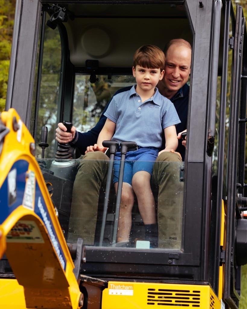 Prince Louis is sitting on The Prince of Wales' lap as Prince William operates a yellow digger.
