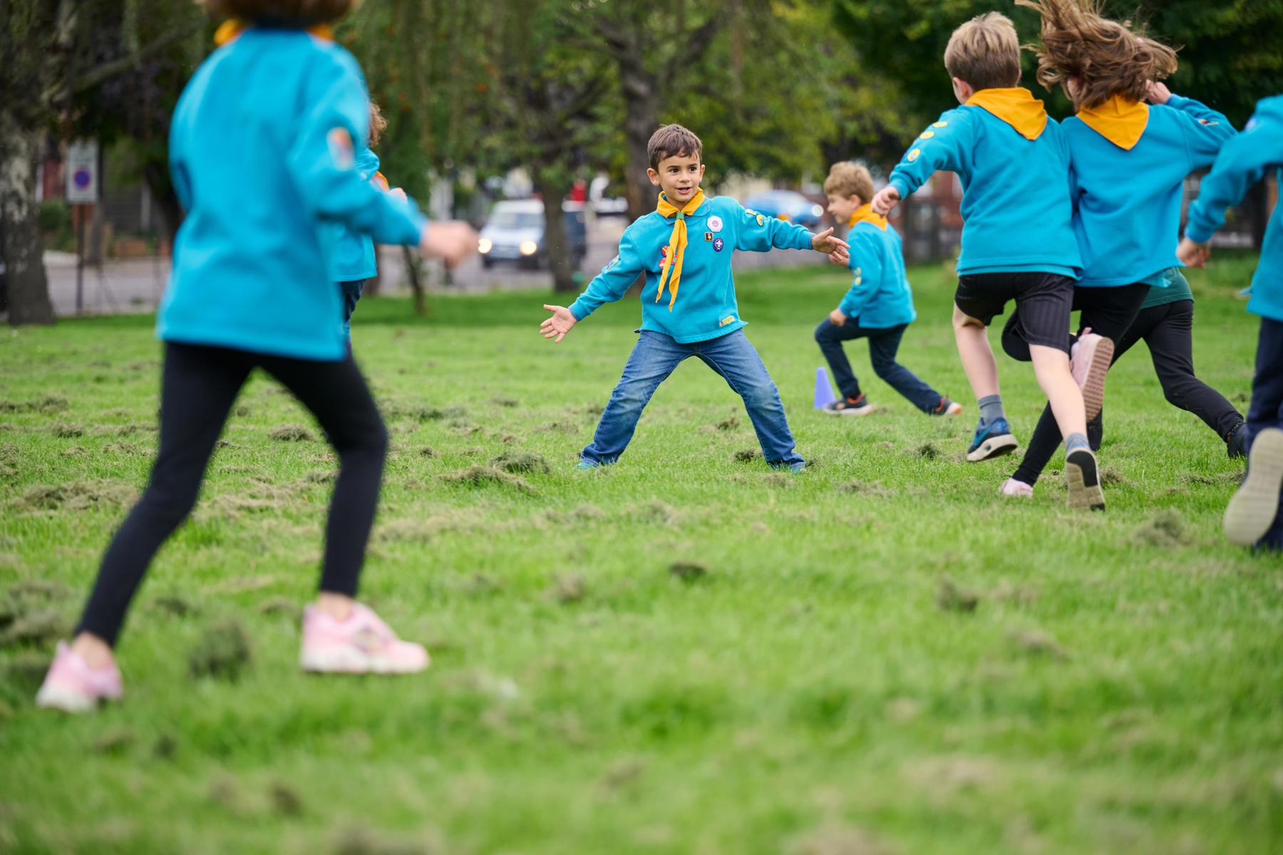 A group of Beavers in blue uniforms and yellow neckers run around on a field playing a game