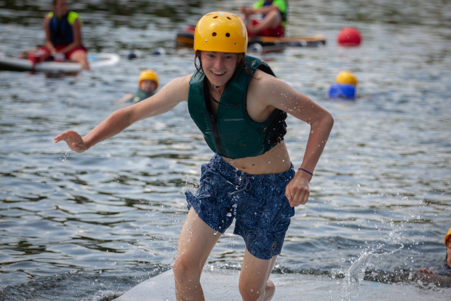 A Scout in a life jacket and helmet smiles as they run on a water obstacle course.