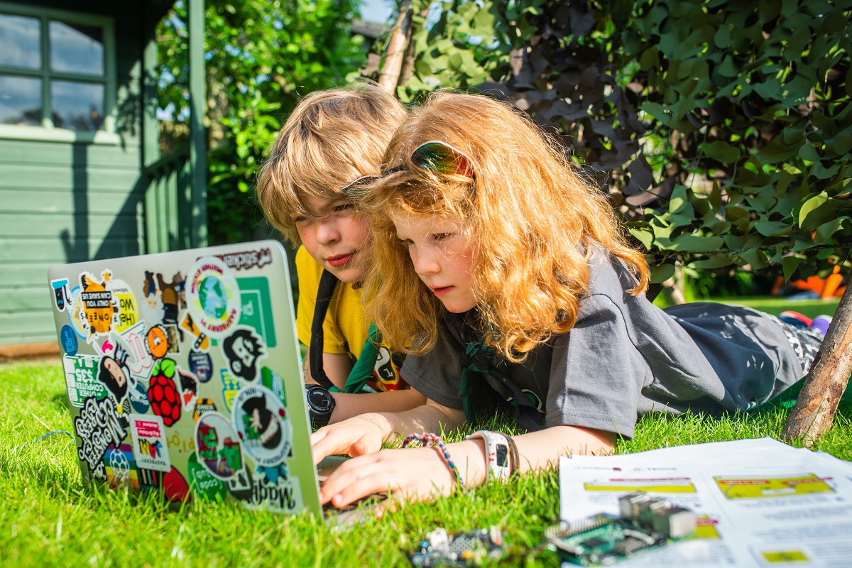 Two young people lying in a garden looking at a laptop full of stickers