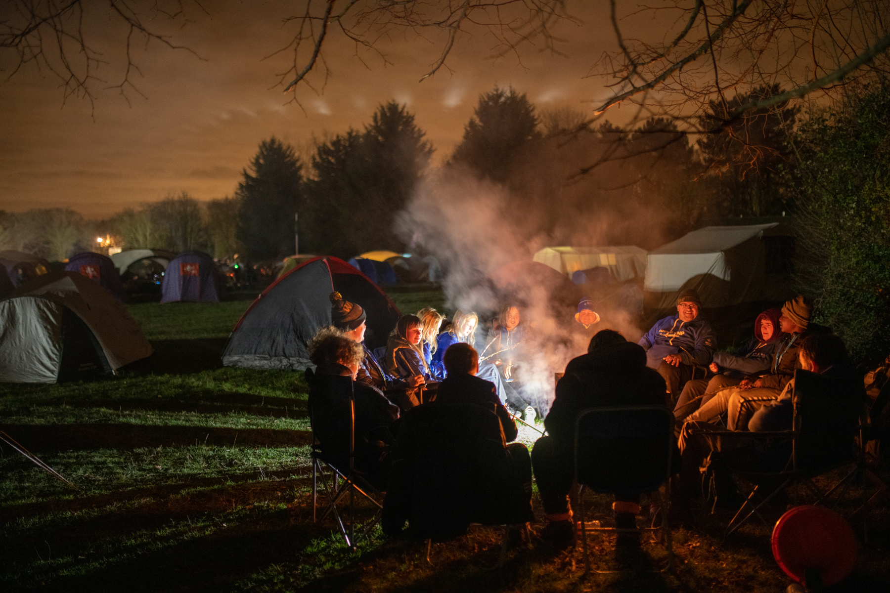 Group of people sitting around a campfire at night