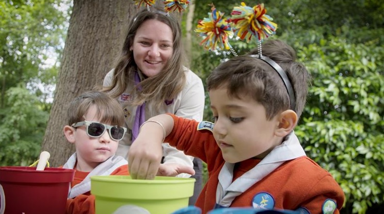 Ninian, a Squirrels volunteer, smiles and watches as two Squirrels play with plant pots.