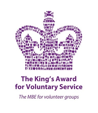The image shows the logo for The King's Award for Voluntary Service. The text 'The King's Award for Voluntary Service' appears beneath a purple crown, with the text 'The MBE for volunteer groups' appearing underneath that.
