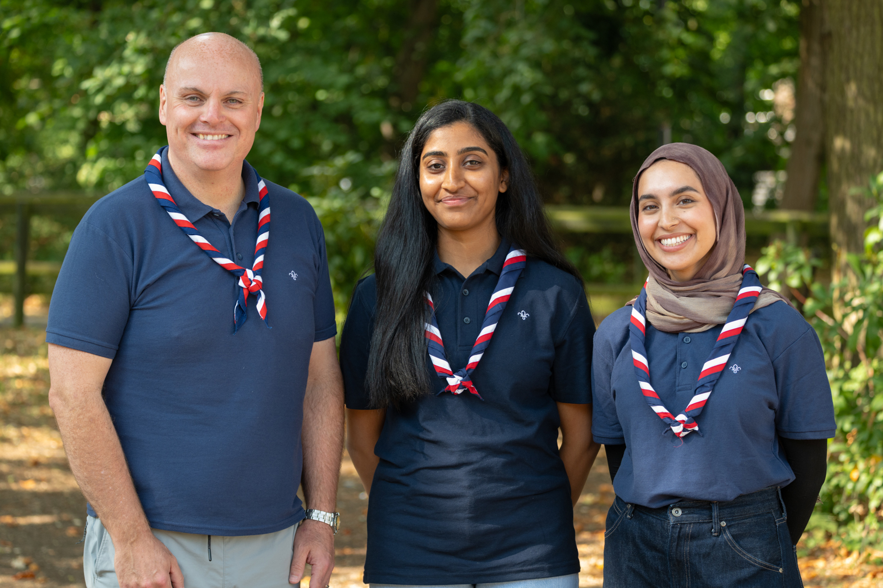 A man, and then two women wearing blue polos and UK neckers, photo taken from waist up