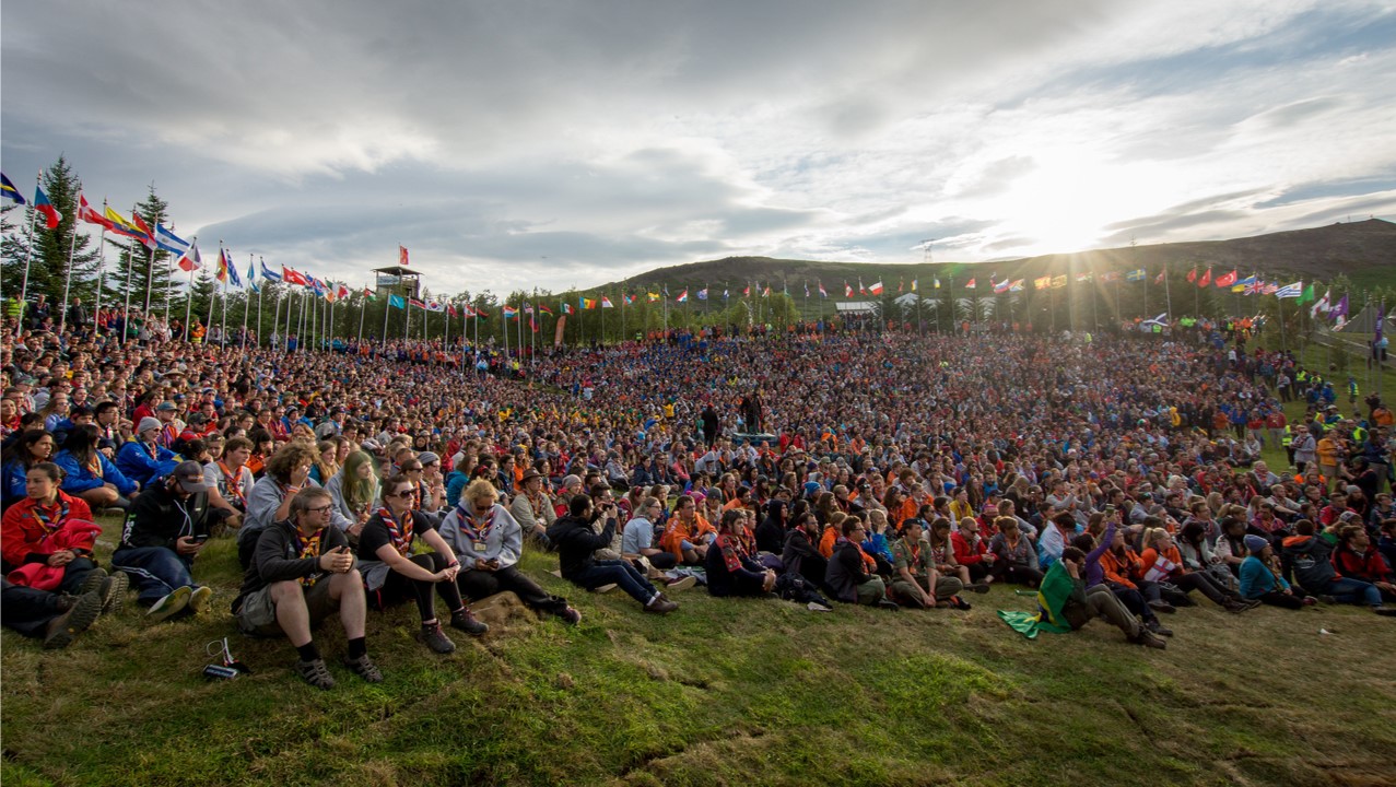 A big group of Scouts sit down an at international campfire in the sunset.