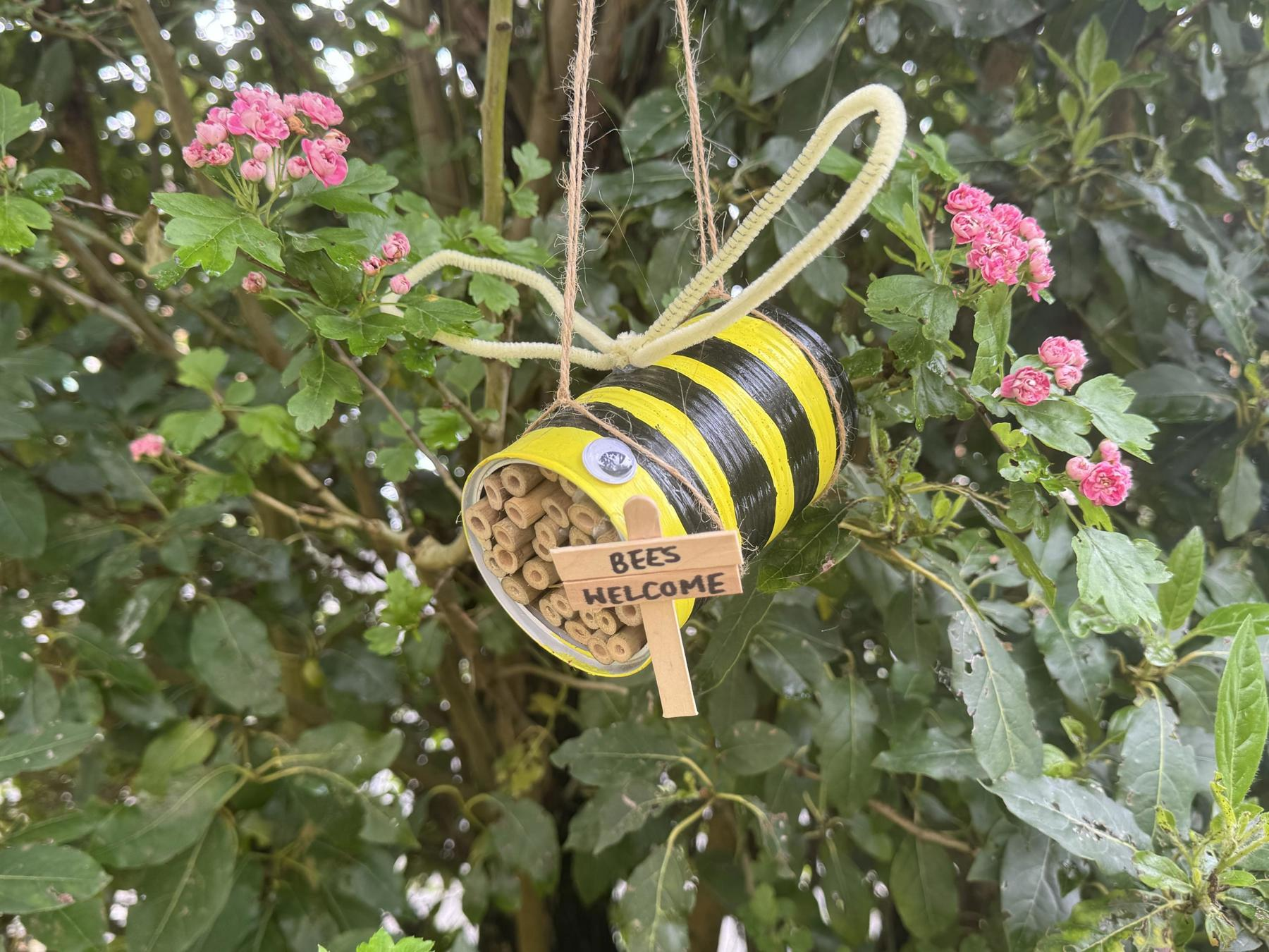 A picture of a bee hotel. It's a tin can, filled with bamboo sticks, that's been painted with black and yellow stripes to look like a bee.