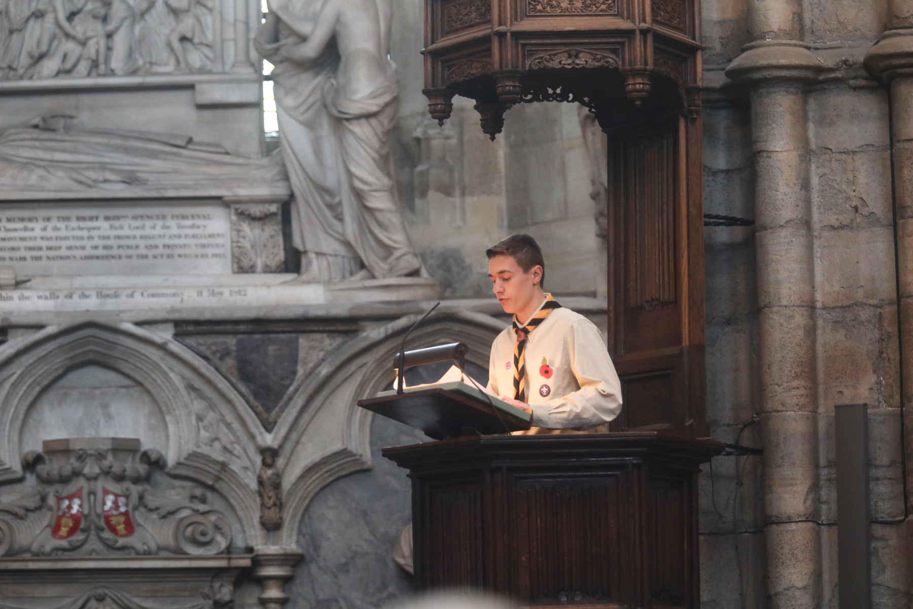 A Scout in uniform stands on the Westminster Abbey pulpit and speaks.