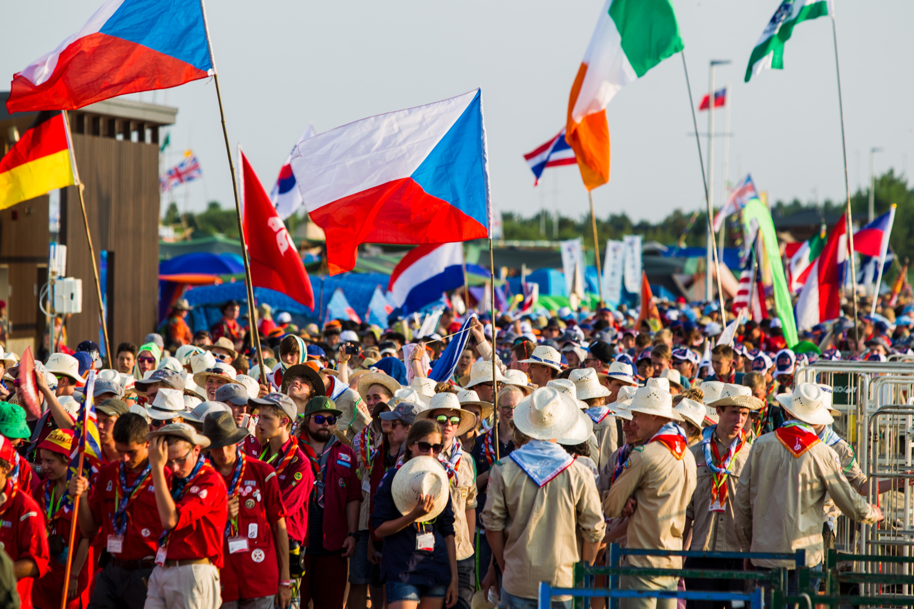 A crowd of scouts at the World Scout Jamboree holding flags on tall flagpoles