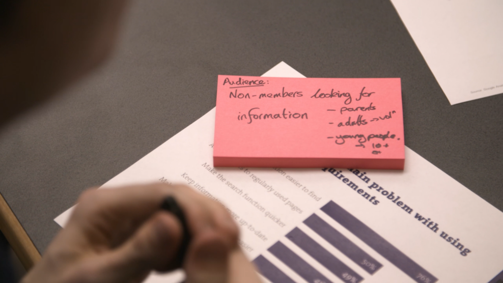 Post it note block on a sheet of paper with a bar graph - image is blurred. Hands in the foreground.