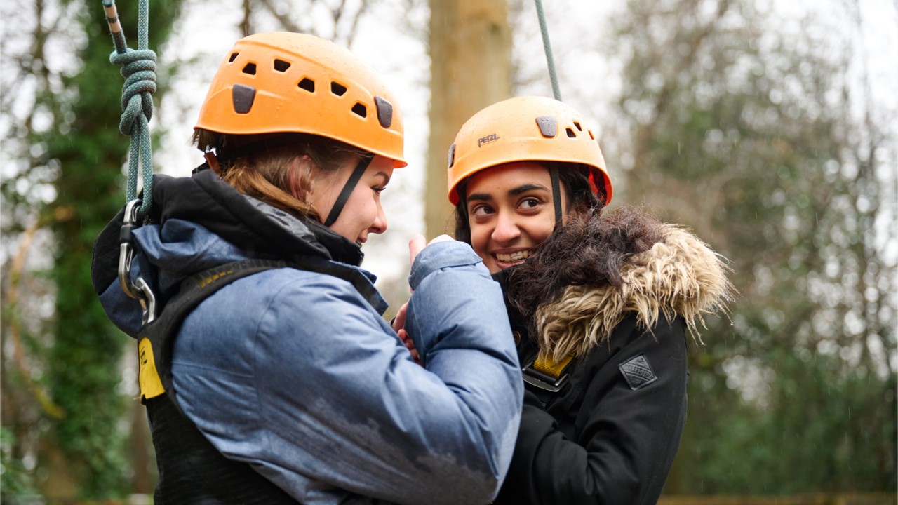 Two young people, both wearing yellow helmets, smile while doing an outdoors activity.