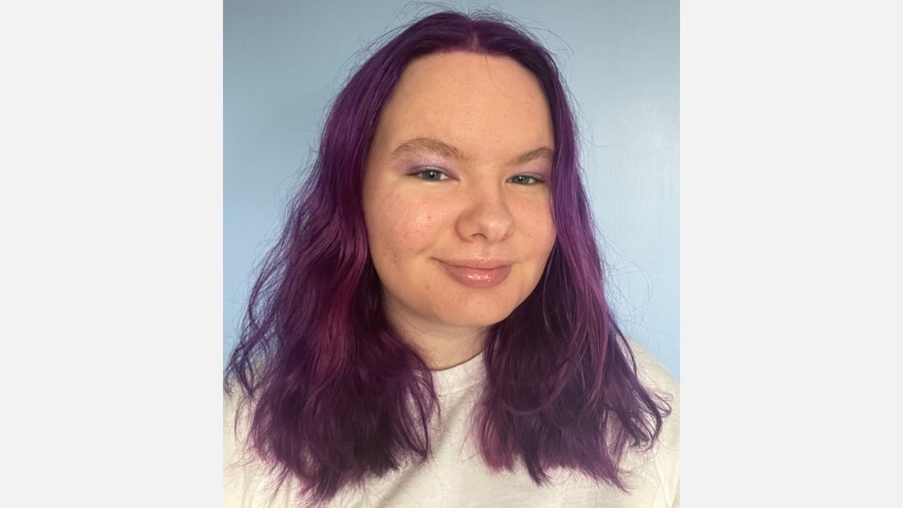 A young person with purple hair and sparkly purple eyeshadow
