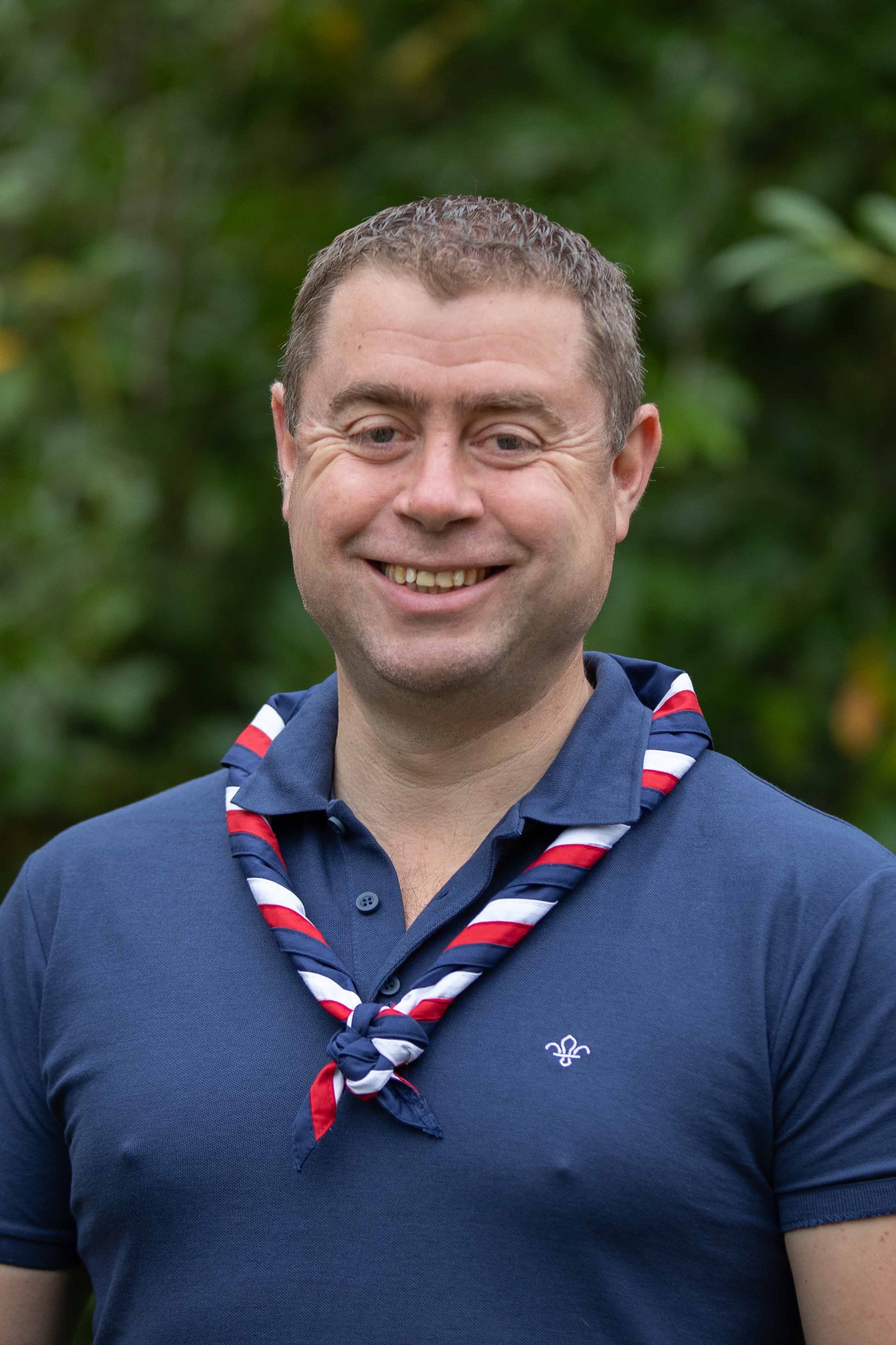 Chris, wearing a navy polo and red, white and blue necker, smiles at the camera.