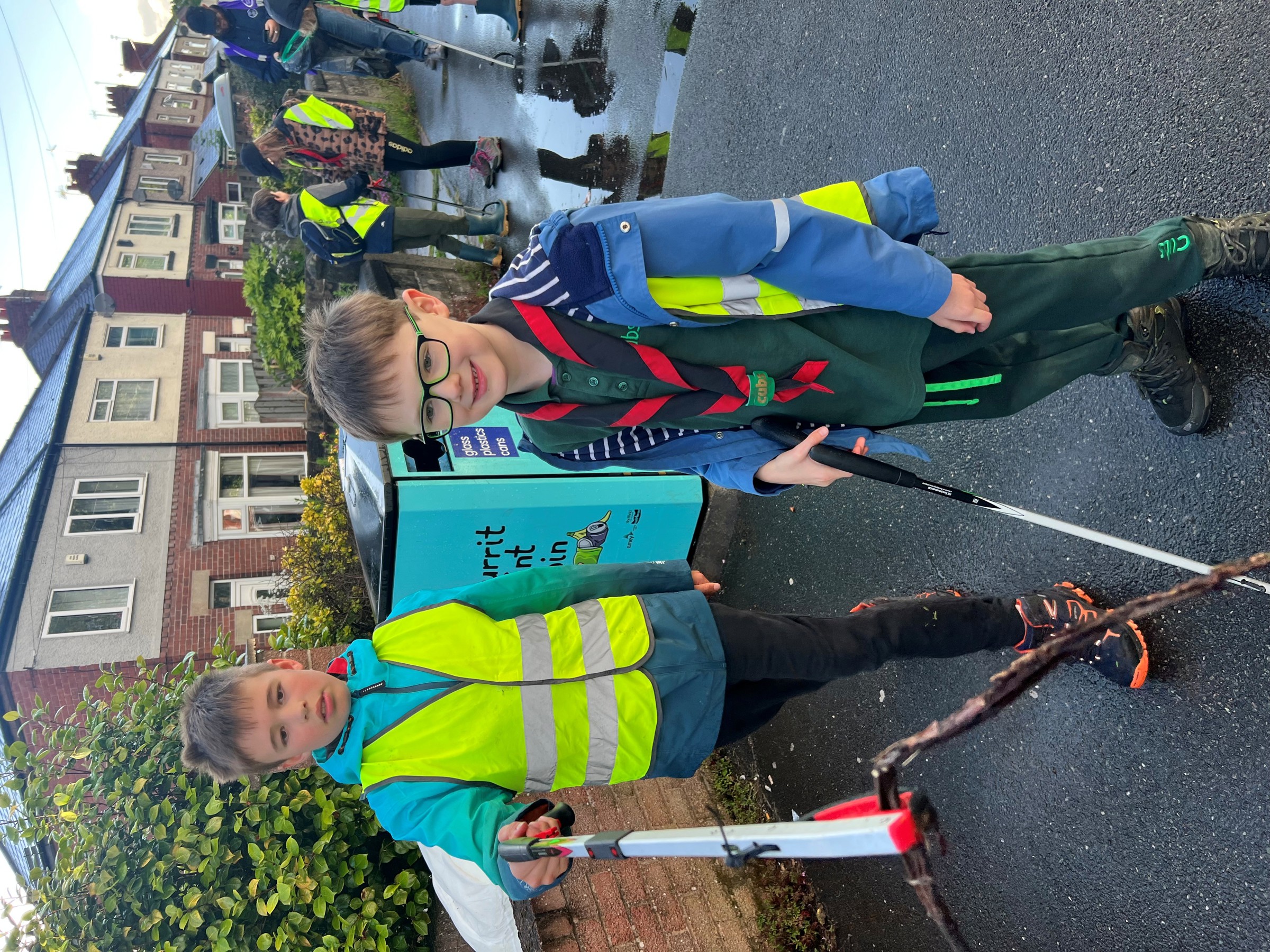 Two young people, wearing high-vis jackets, pick up litter.