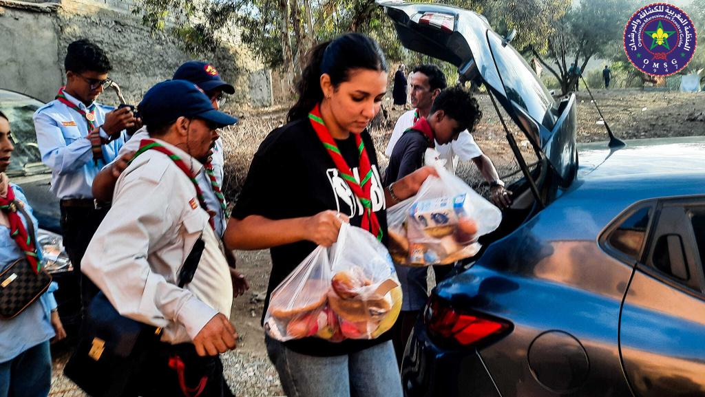 Scouts in Morocco are in uniform and neckers and are carrying bags of groceries out of a car boot to help those affected by the earthquake.