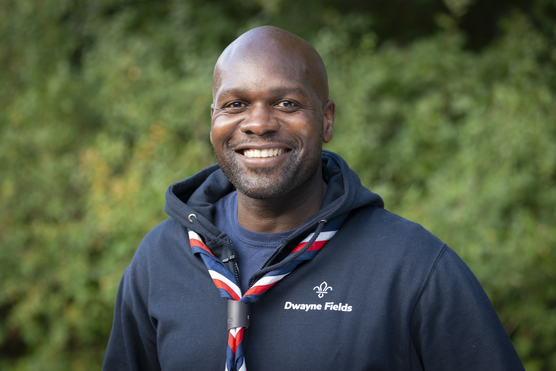 Image shows Dwayne Fields in a necker and hoodie smiling in Gilwell Park